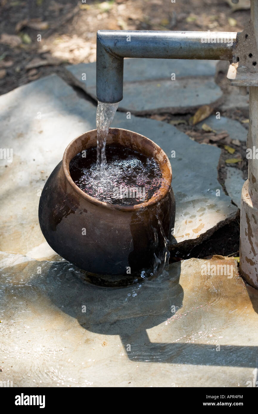 Remplissage d'un pot en argile avec de l'eau à une pompe à main dans la campagne indienne. L'Andhra Pradesh. L'Inde Banque D'Images