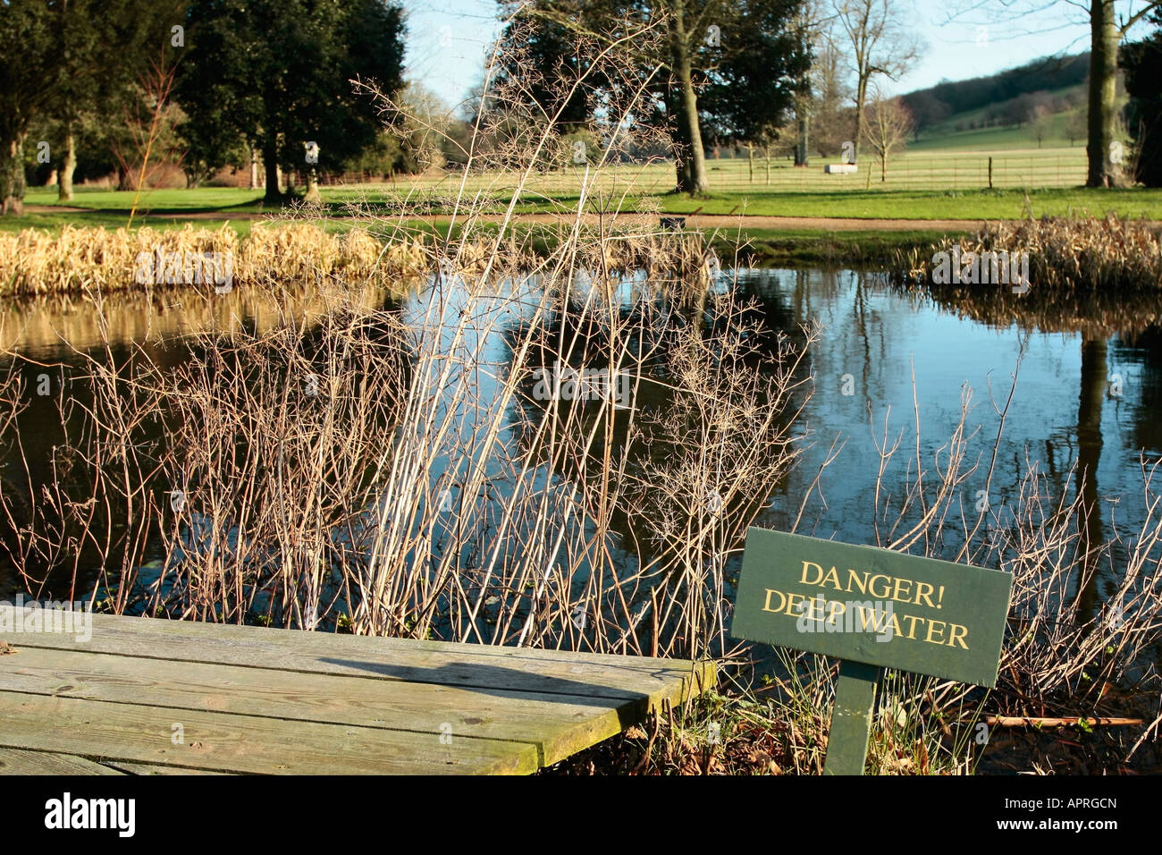 Étang en fin d'hiver avec le panneau d'avertissement « danger Deep Water » sur le bord. West Dean Gardens, Sussex, Angleterre, Royaume-Uni Banque D'Images