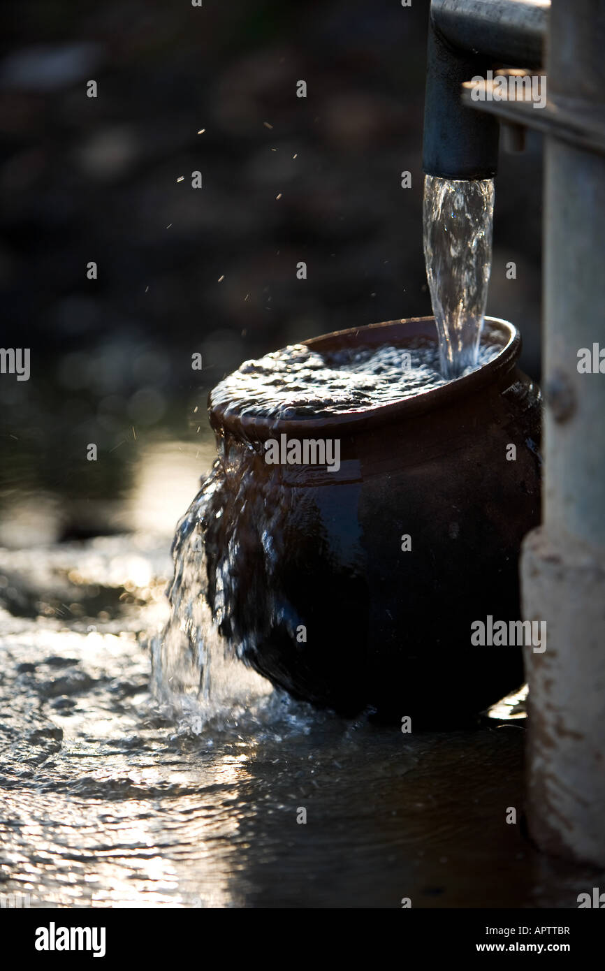 Remplissage d'un Indian Clay pot avec de l'eau propre et fraîche à une pompe à eau à main dans la campagne indienne. L'Andhra Pradesh, Inde Banque D'Images