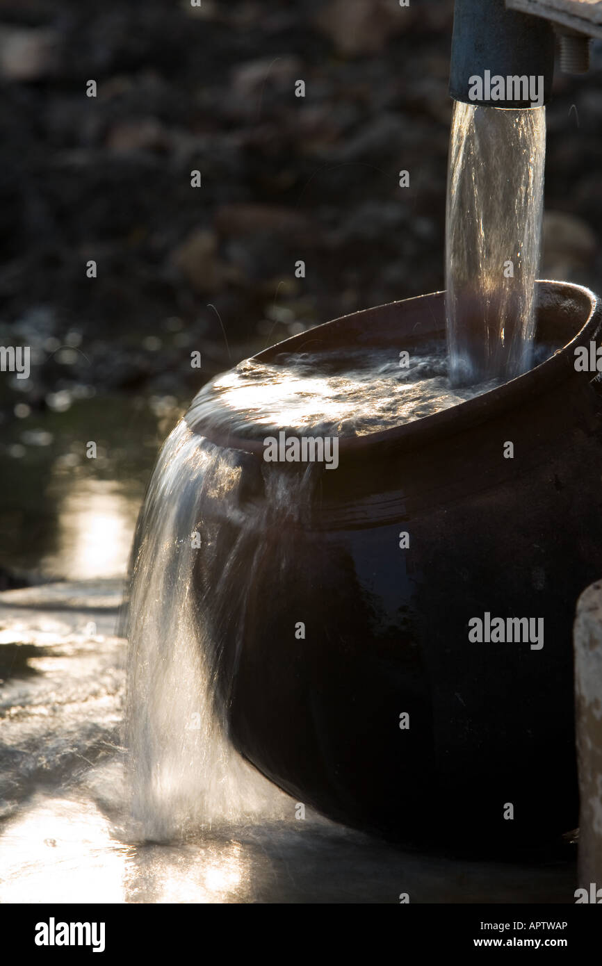 Remplissage d'un Indian Clay pot avec de l'eau propre et fraîche à une pompe à eau à main dans la campagne indienne. L'Andhra Pradesh, Inde Banque D'Images
