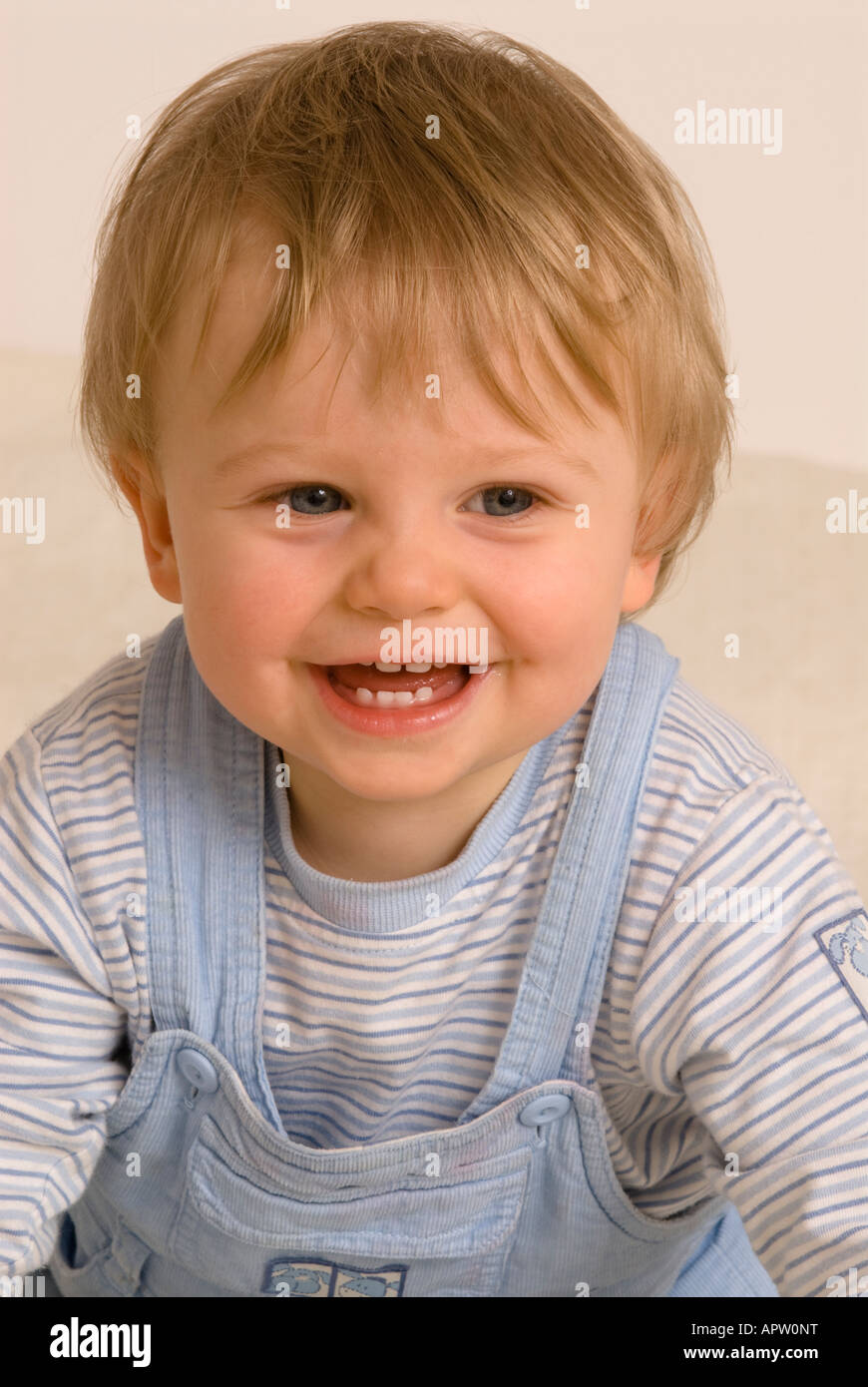 Bébé garçon d'un an regardant la caméra rire souriant bouche heureuse ouverte habillée de T-shirt bleu et salopette, dents de bébé Banque D'Images