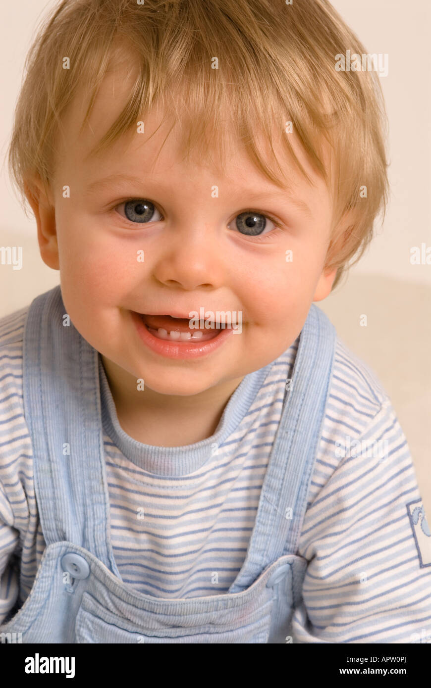 Bébé garçon d'un an regardant la caméra rire souriant bouche heureuse ouverte habillée de T-shirt bleu et salopette, dents de bébé Banque D'Images