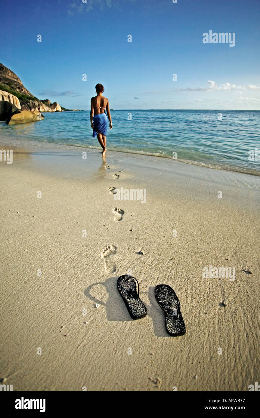 Woman walking down beach à la mer et les empreintes de chaussures parution Modèle Anse Source d'argent beach l'île de La Digue Seychelles Banque D'Images
