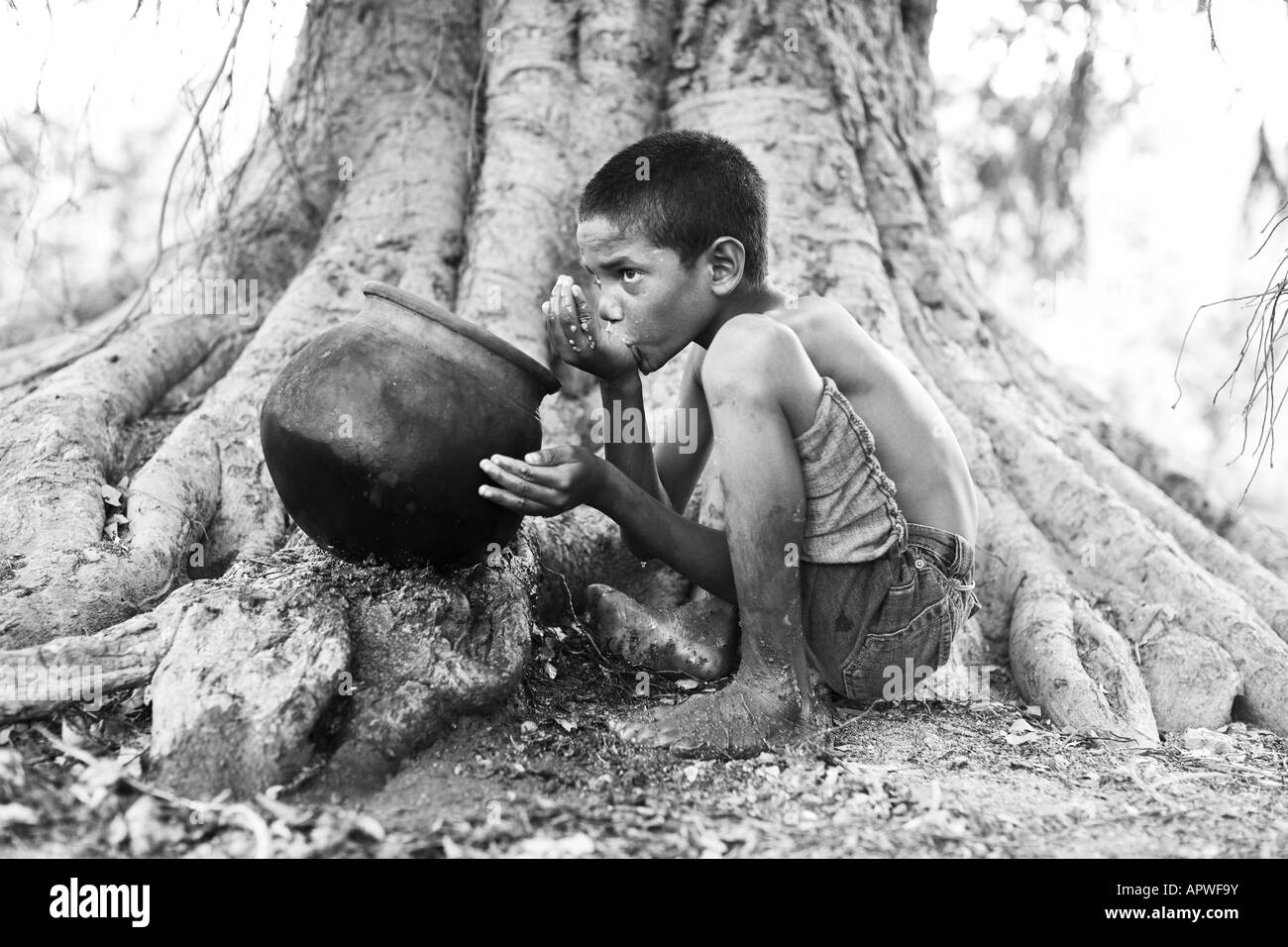 Jeune Indien l'eau potable à partir d'un pot en argile sur Banyan Tree. L'Andhra Pradesh, Inde. Le noir et blanc Banque D'Images