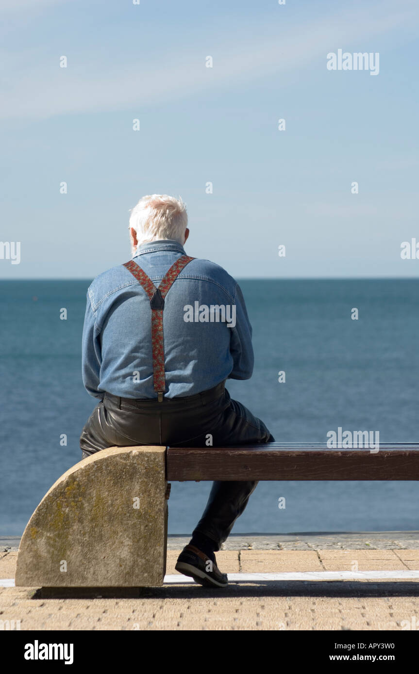 Un seul homme aux cheveux blancs âgés vus de dos assis sur un banc de la promenade d'Aberystwyth après-midi d'été chemise bleue et accolades Banque D'Images