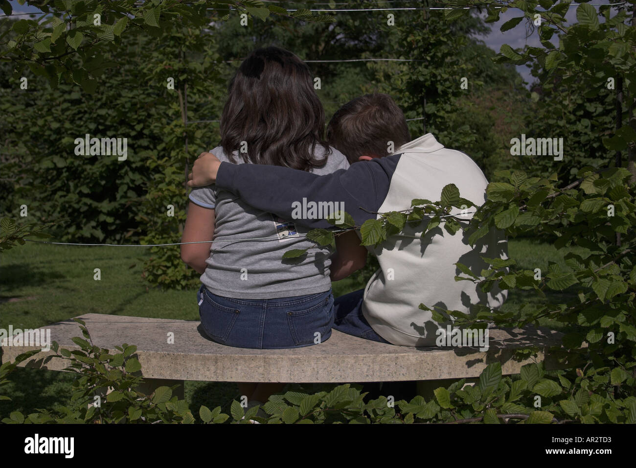 10 ans garçon et fille assise dans un jardin - le garçon a son bras autour de la jeune fille Banque D'Images