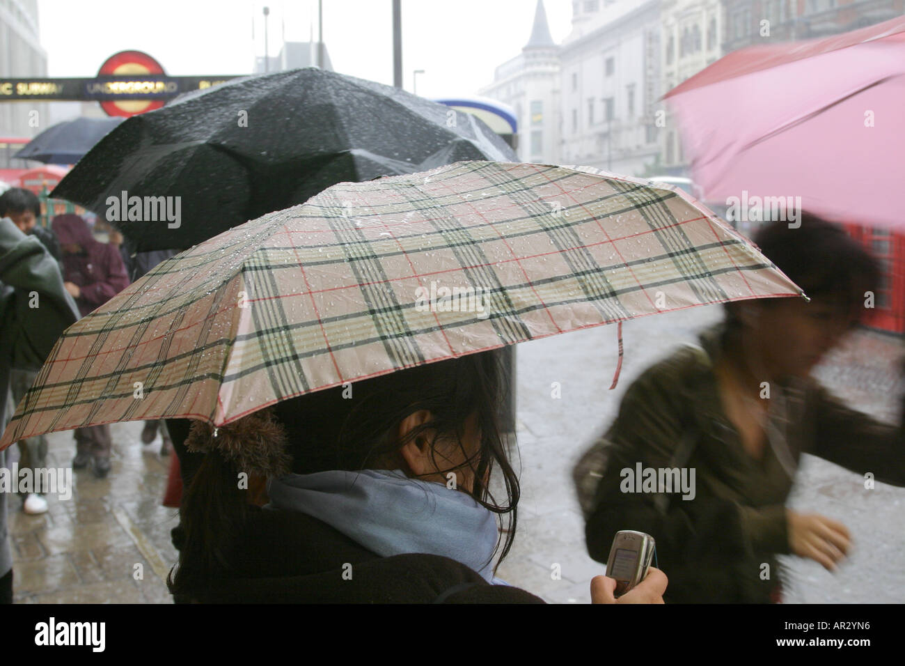 Une femme vérifie son téléphone mobile tenant un parapluie lors d'une forte averse de pluie, Tottenham Court Road, Londres, Royaume-Uni. L'année 2006. Banque D'Images