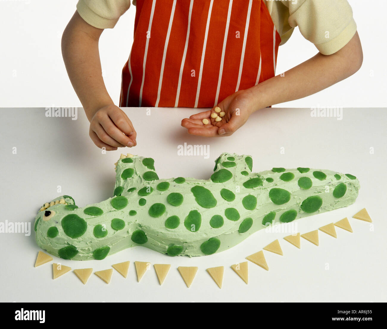 Modele Main Portant Un Tablier A Rayures Orange Et Blanc Decoration Gateau En Forme De Dinosaure Vert Avec Boutons Chocolat Blanc Photo Stock Alamy