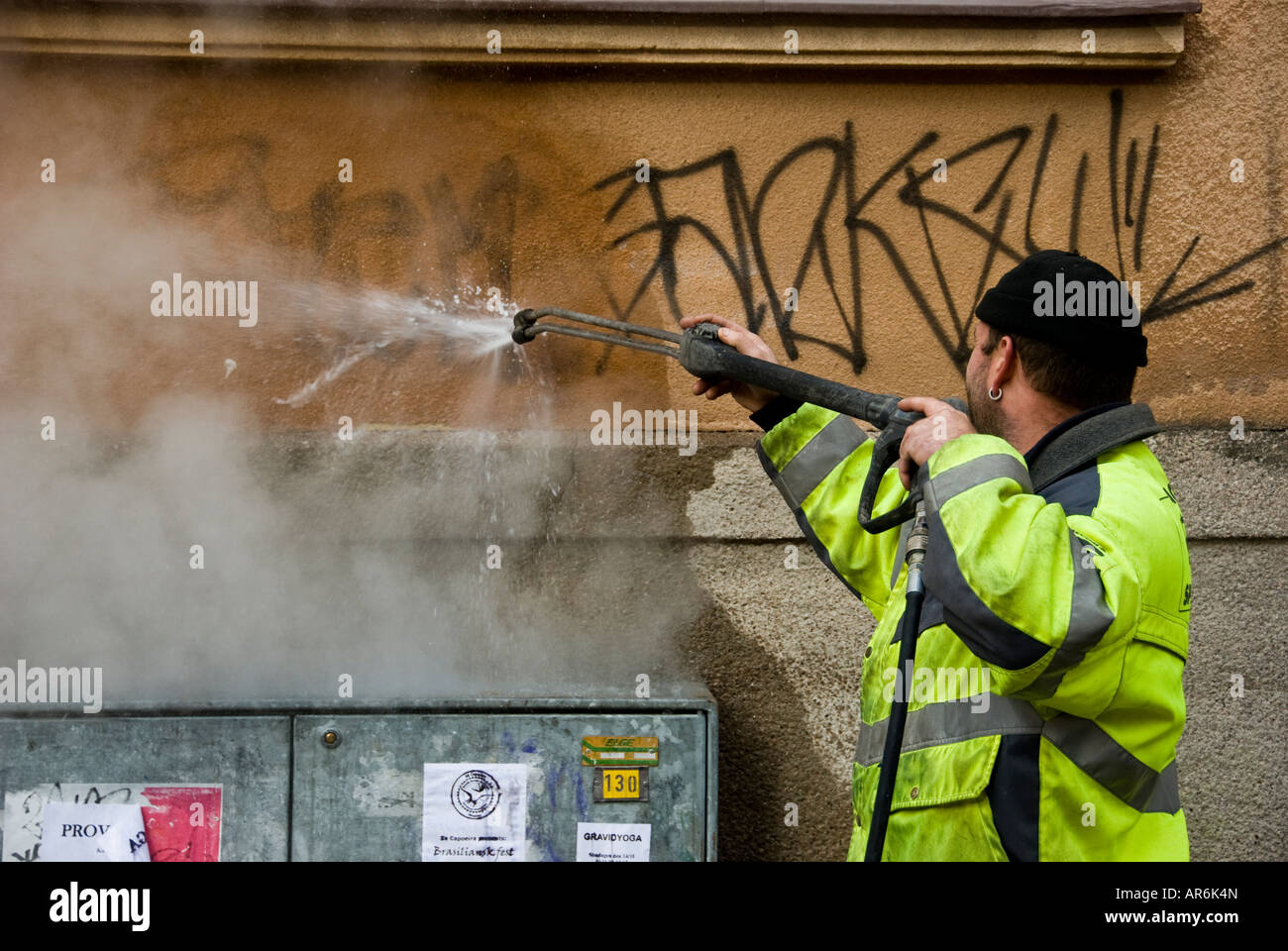 Un travailleur de l'assainissement tente de nettoyer un mur de graffiti avec un tuyau d'eau haute pression Banque D'Images