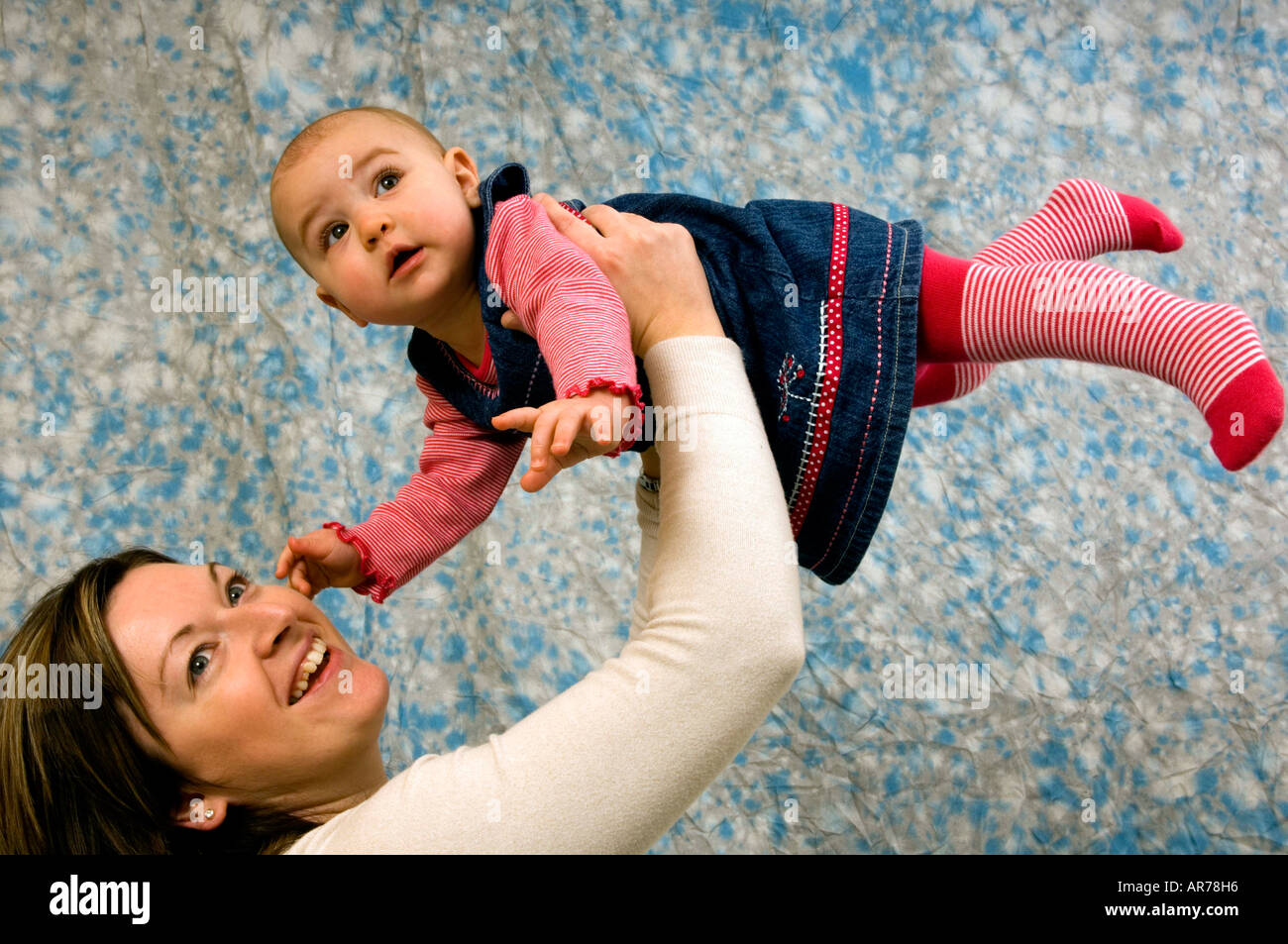 Un portrait d'une jeune femme âgée de six mois bébé bébé être jetée dans l'air par sa mère en souriant. Banque D'Images