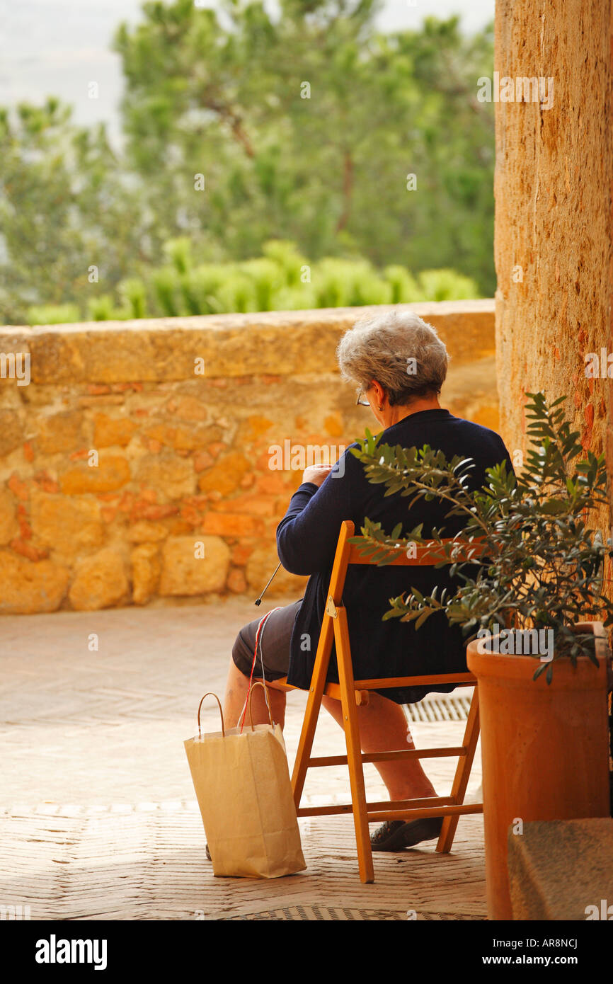 Senior lady knitting devant sa maison, Pienza, Toscane, Italie Banque D'Images