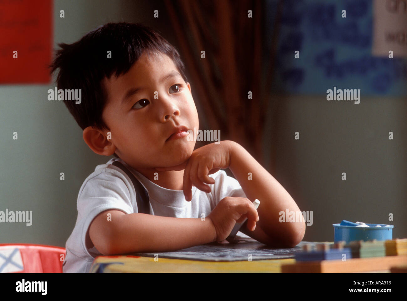 SALLE DE CLASSE POUR ENFANTS CORÉENS CHERCHANT À APPRENDRE garçon oriental âgé de 4-5 ans assis dans la classe de MATERNELLE concentrant l'attention. Lumière naturelle de la fenêtre Banque D'Images
