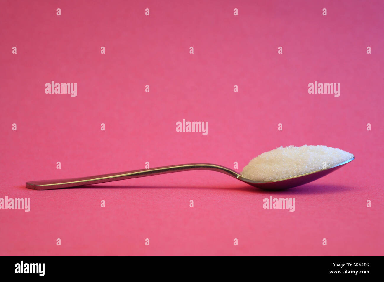 Cuillerée de sucre blanc contre un fond rose. Banque D'Images