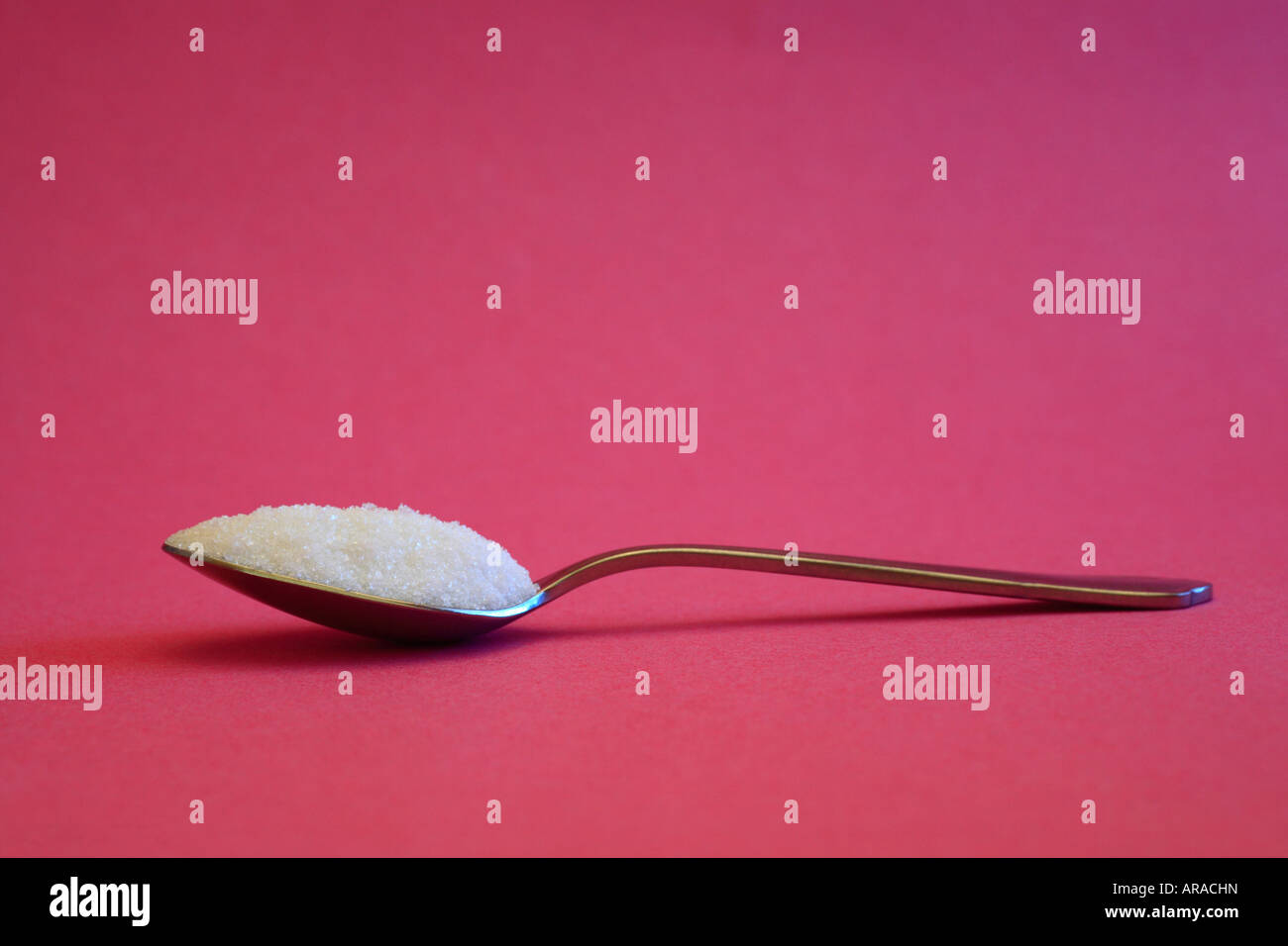 Cuillerée de sucre blanc contre un fond rose. Banque D'Images