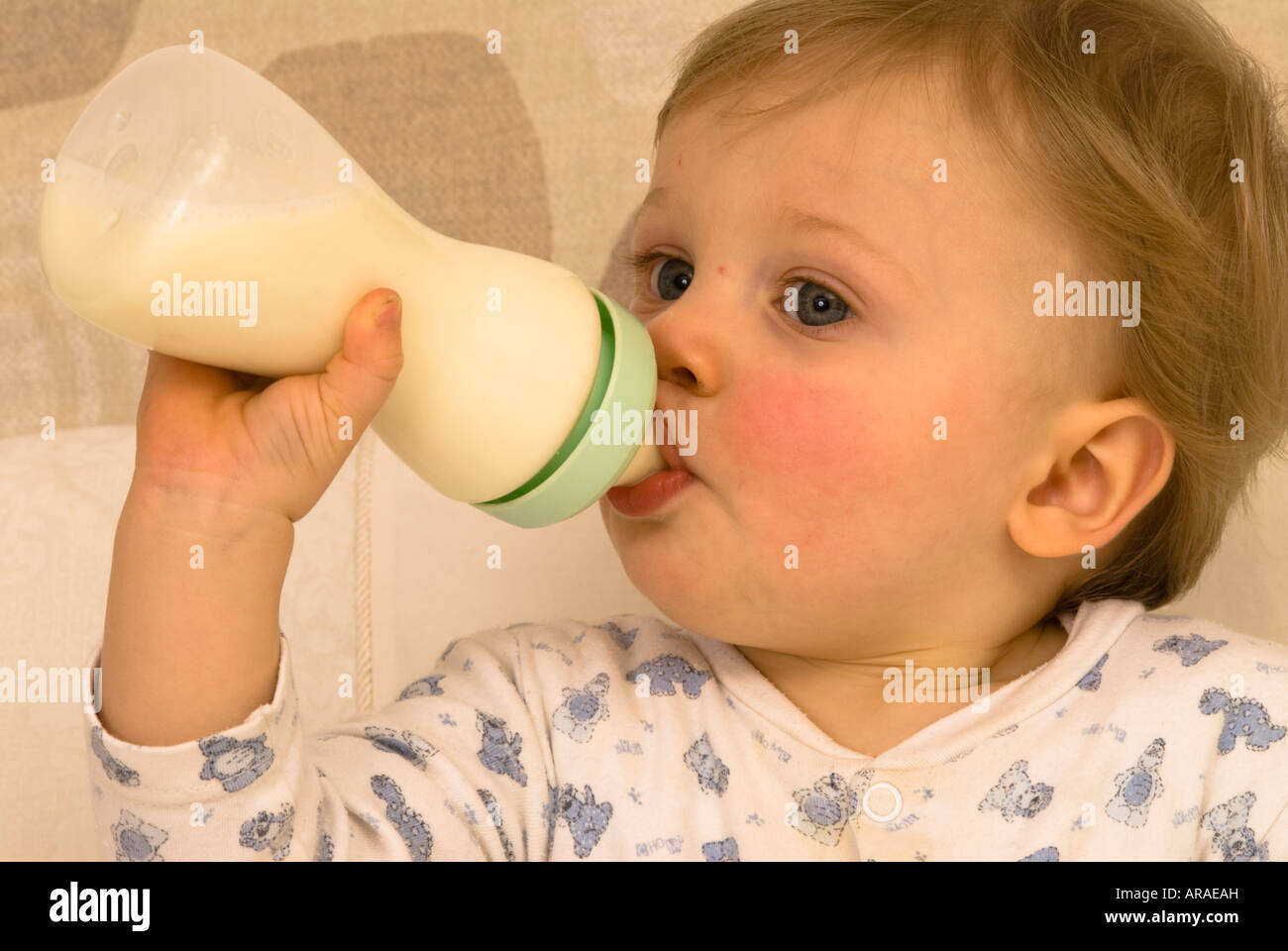 Bébé garçon d'un an tenant et buvant de son biberon du lait habillé pour le lit Banque D'Images