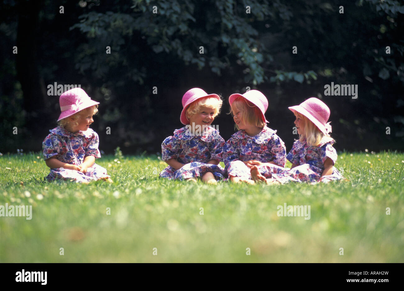 4 filles assis dans l'herbe avec chapeaux rose Banque D'Images