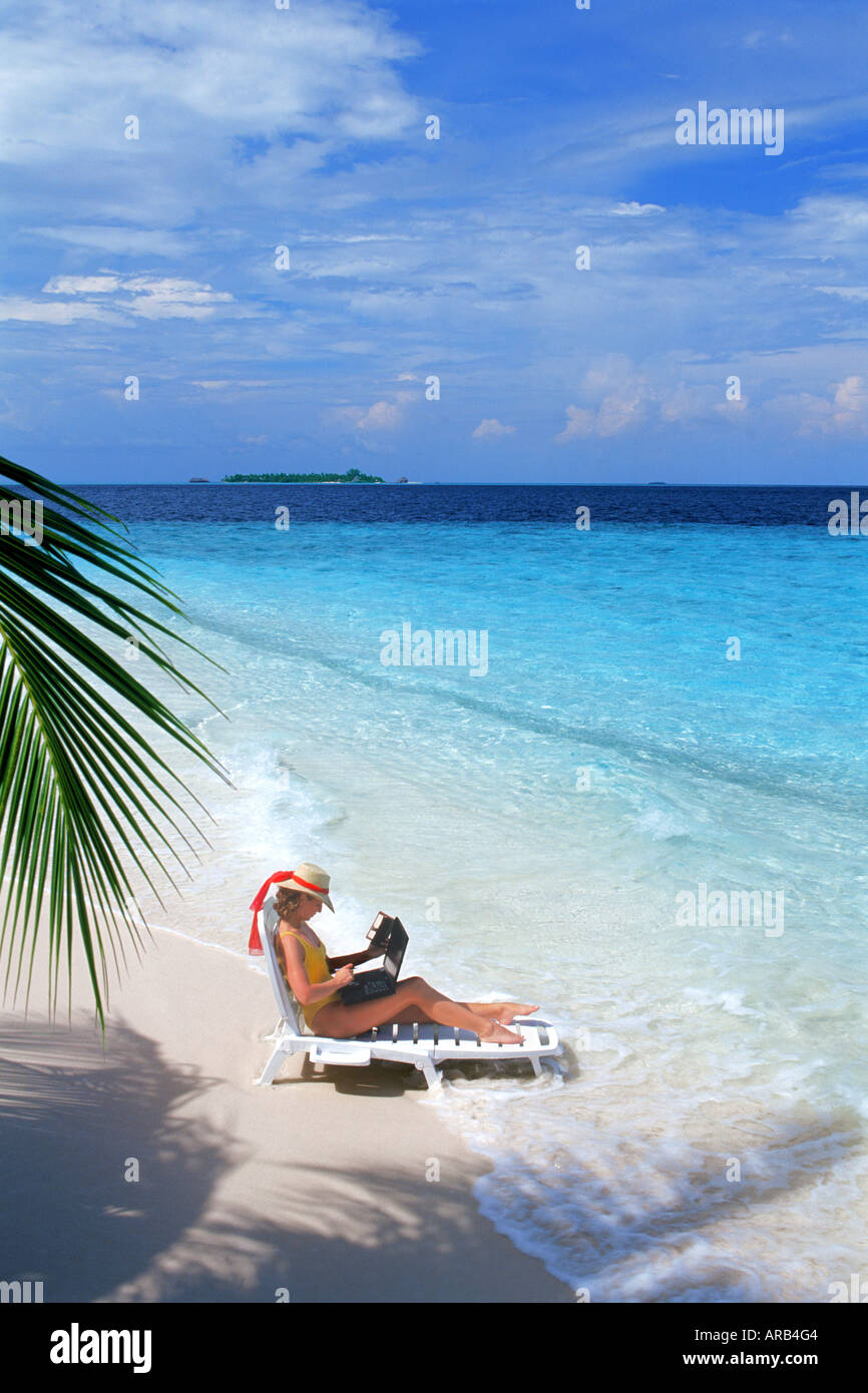 Femme assise sur sandy shore sur chaise de plage avec ordinateur portable pendant les vacances Banque D'Images
