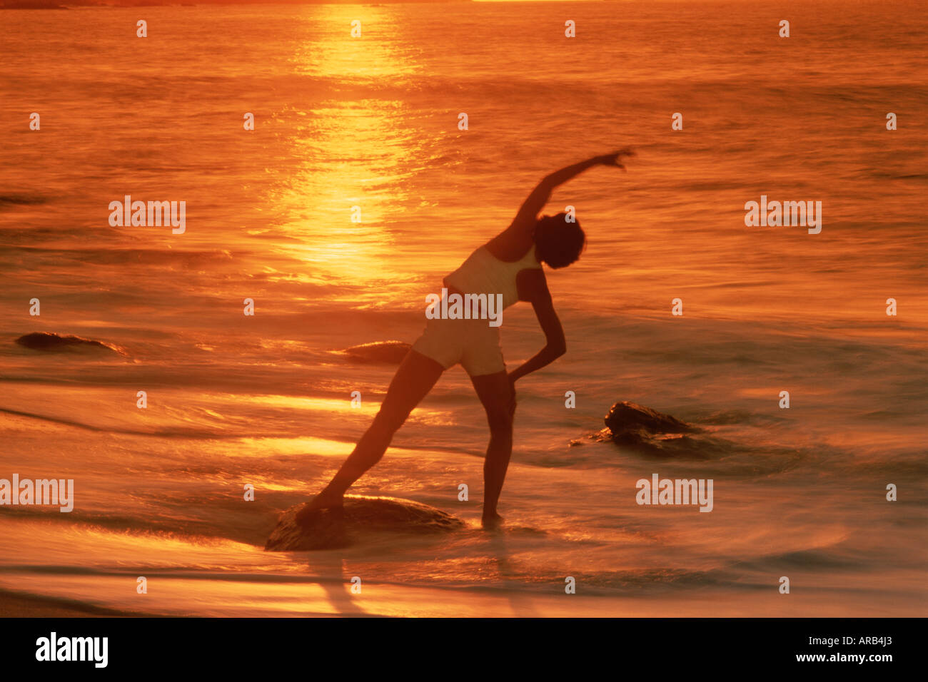 Woman in yoga position sur la plage au coucher du soleil Banque D'Images