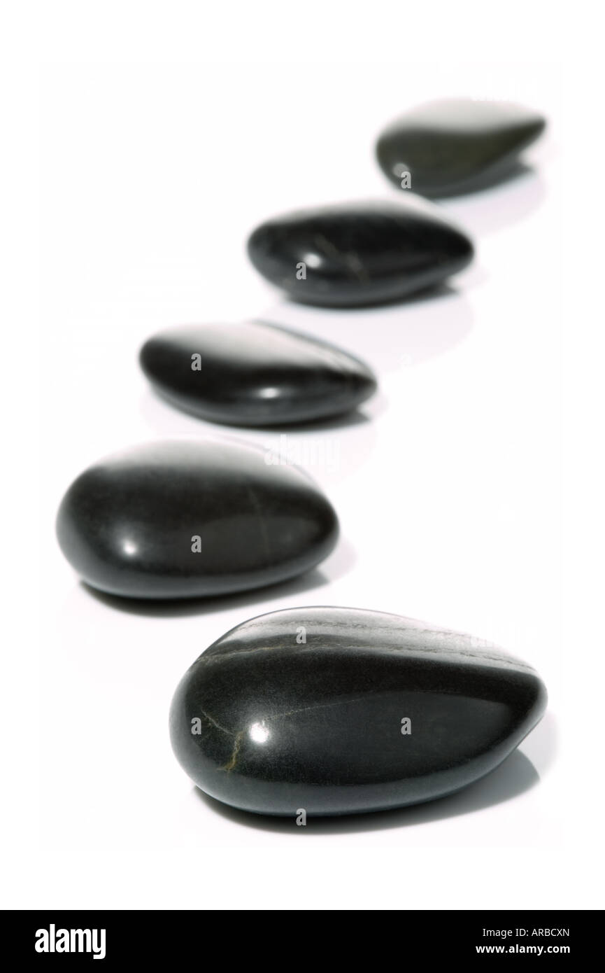Cinq cailloux noirs dans une légère courbe sur une surface blanche avec réflexion High key shot avec profondeur de champ Banque D'Images