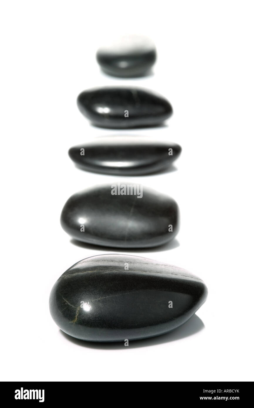 Cinq cailloux noirs dans une rangée verticale sur une surface blanche avec réflexion High key shot Banque D'Images