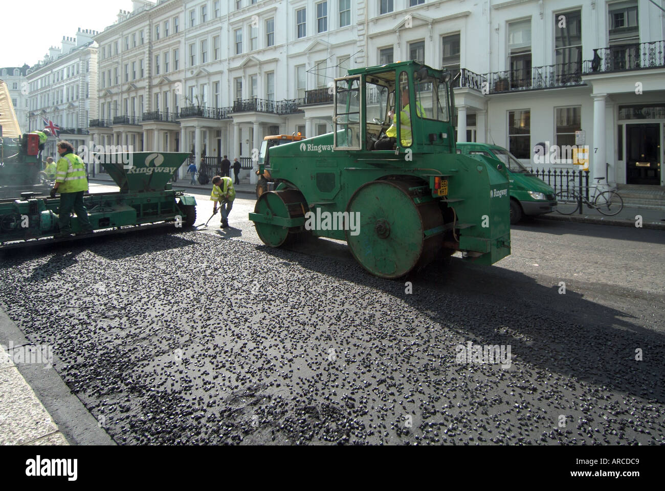 Contra Jour contre l'éclairage de jour sur les hommes et les machines au travail avec de grands rouleaux posant une nouvelle surface de route tarmac dans South Kensington Londres Angleterre Royaume-Uni Banque D'Images