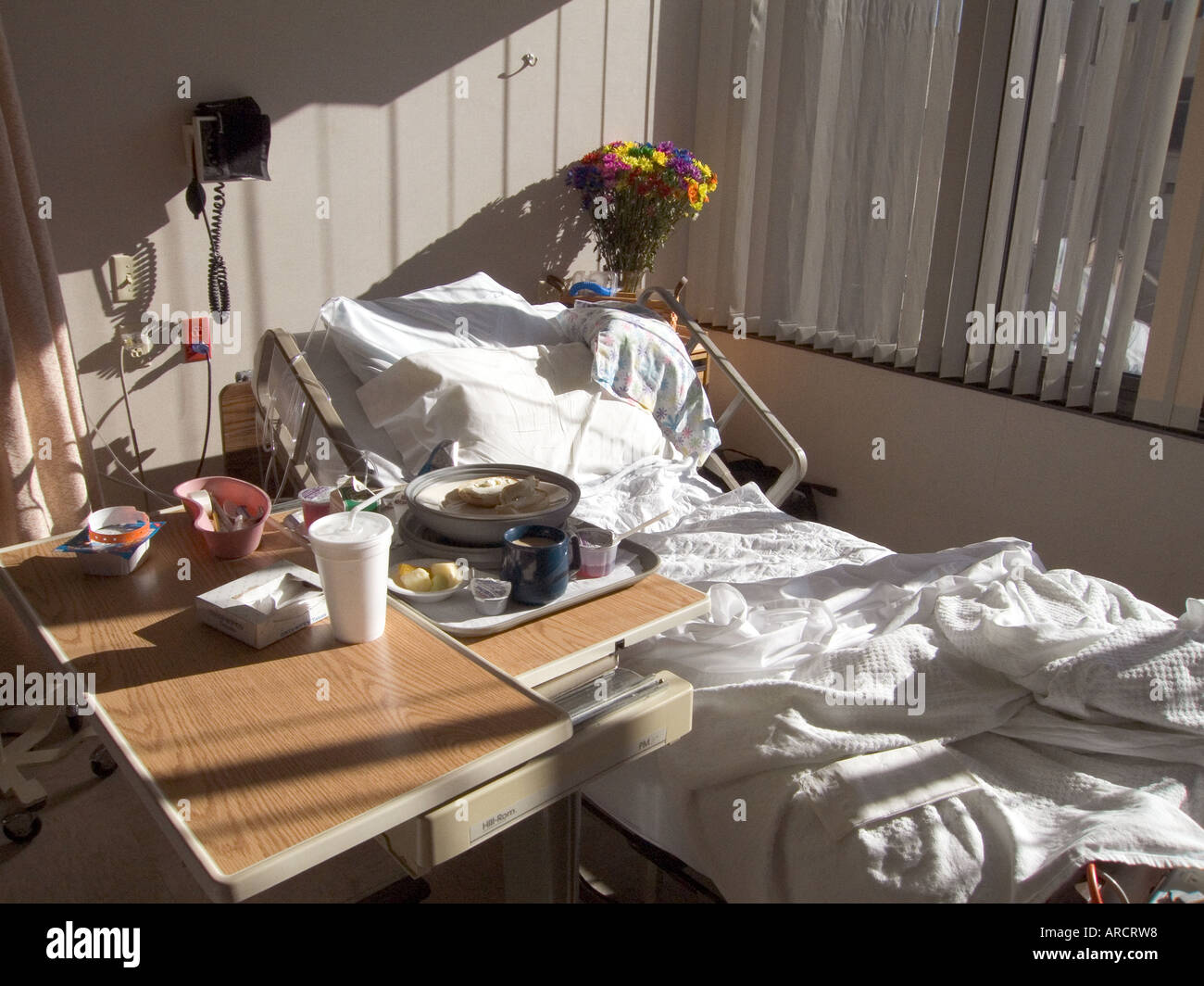 Un patient dans son lit éclairé par le soleil du matin. La photo montre un plateau de petit-déjeuner et d'un vase de fleurs à la tête du lit. Banque D'Images