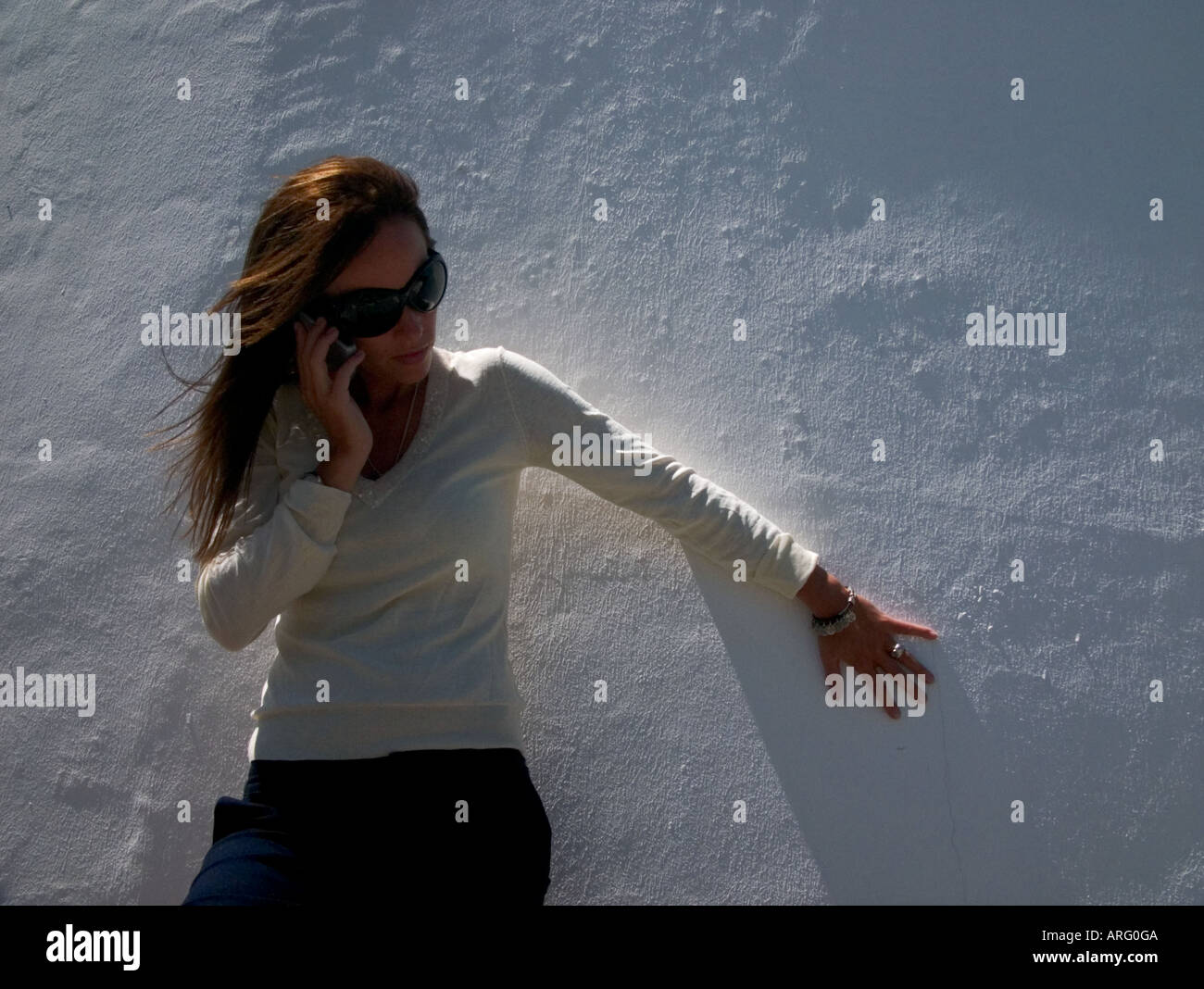 Un low angle view of young woman leaning against a white mur incurvé en conversation sur son mobile Banque D'Images