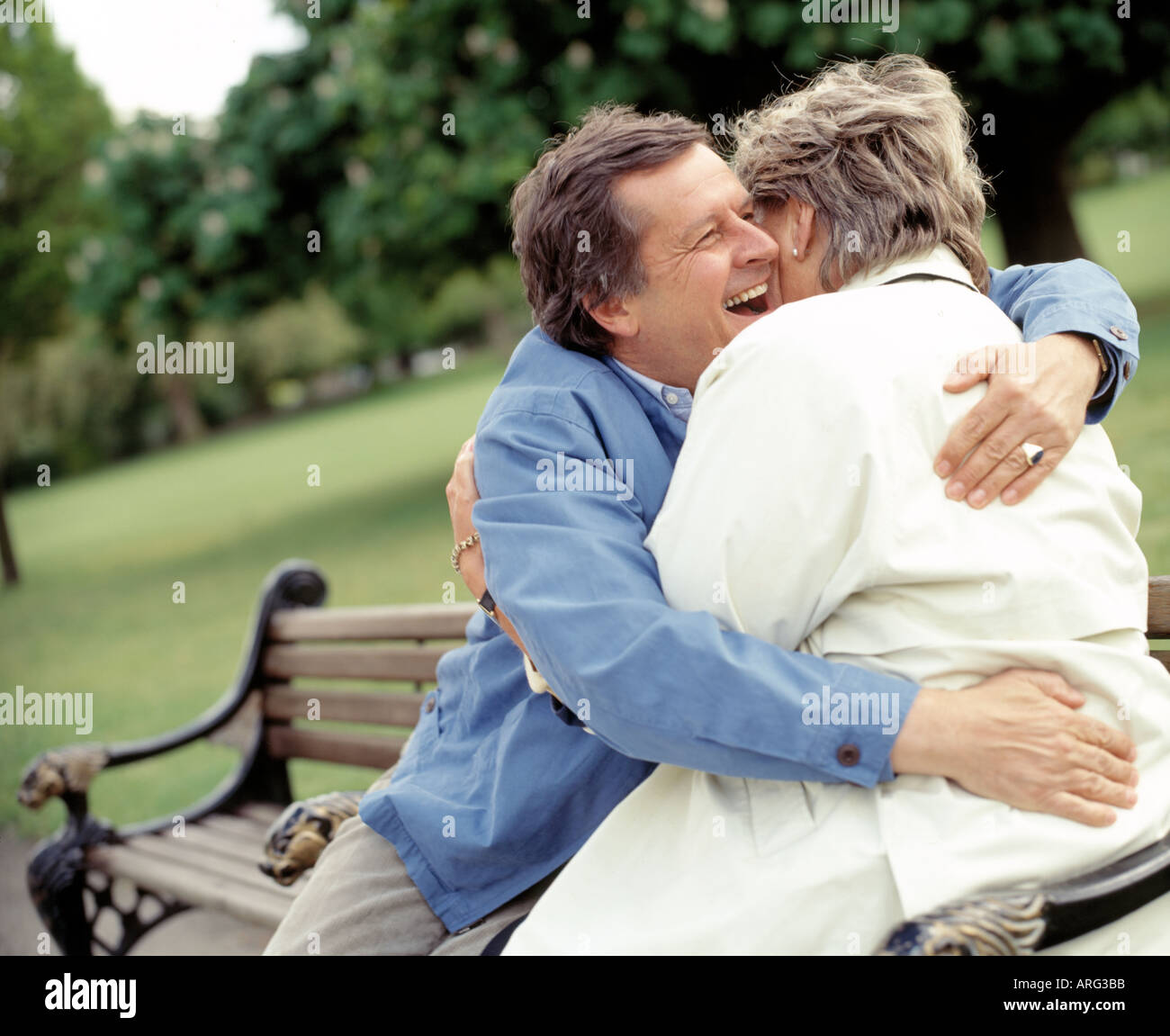 Moyen âge couple laughing et hugging on park bench Banque D'Images
