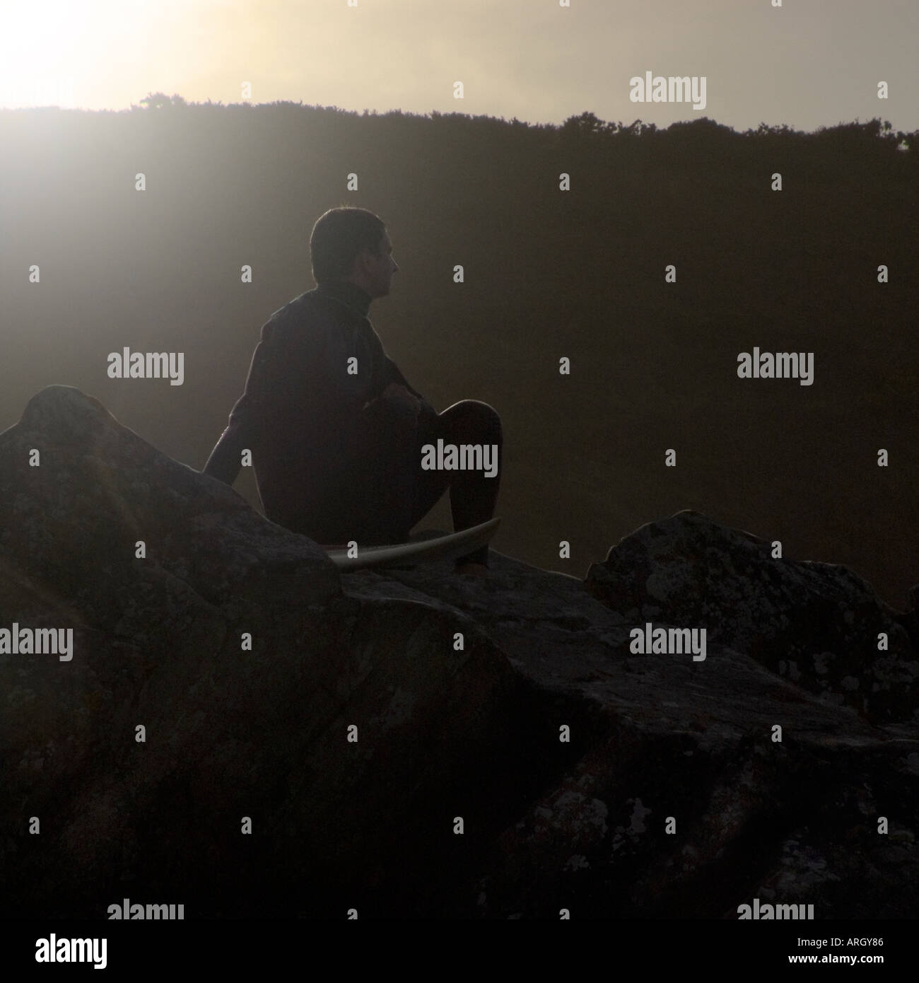 Un surfeur assis à Woolacombe Bay attendant et contemplant sa prochaine vague. North Devon Angleterre Royaume-Uni Banque D'Images