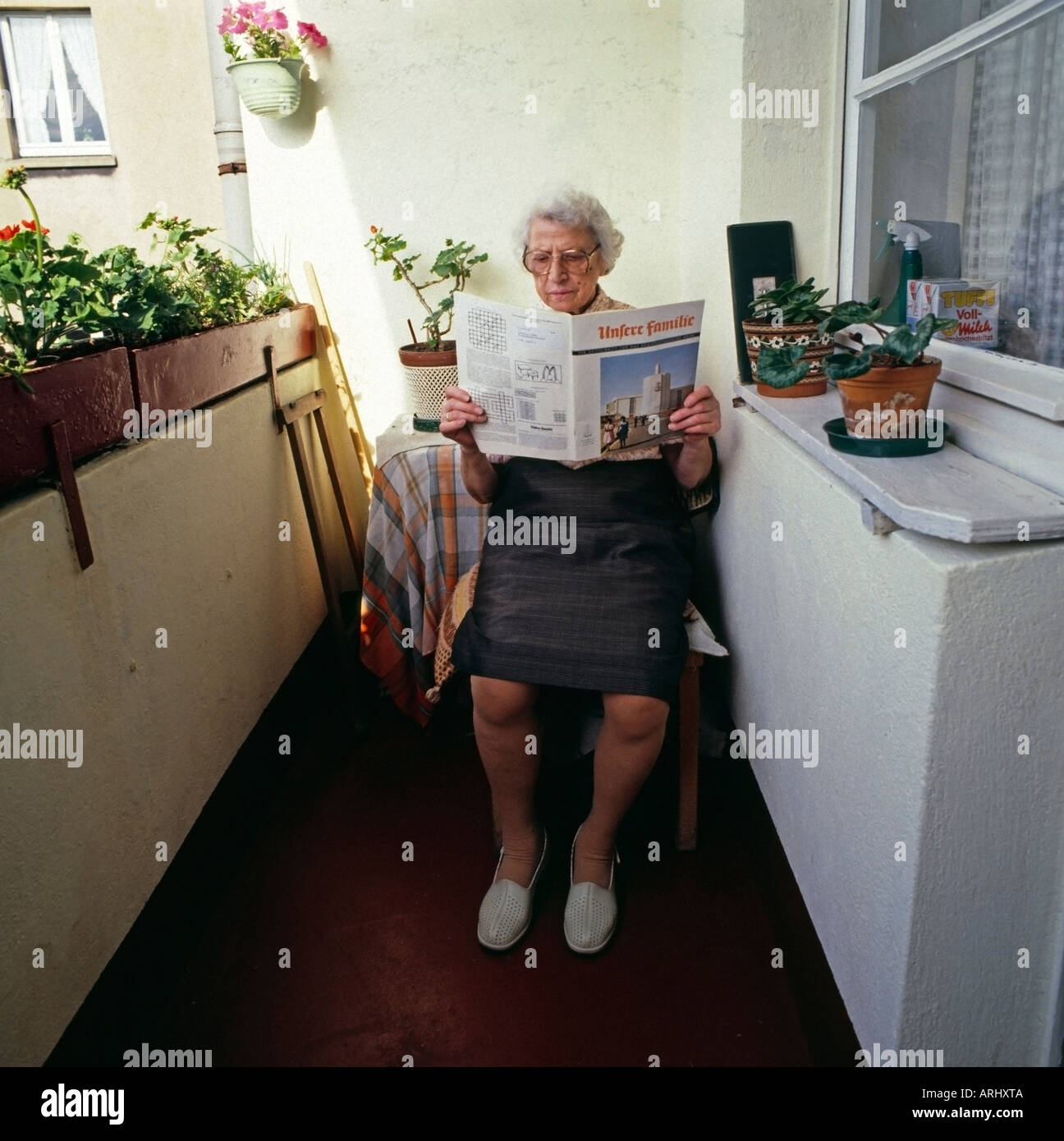 Vieille Femme assise sur le balcon de la lecture d'un magazin de bureau Banque D'Images