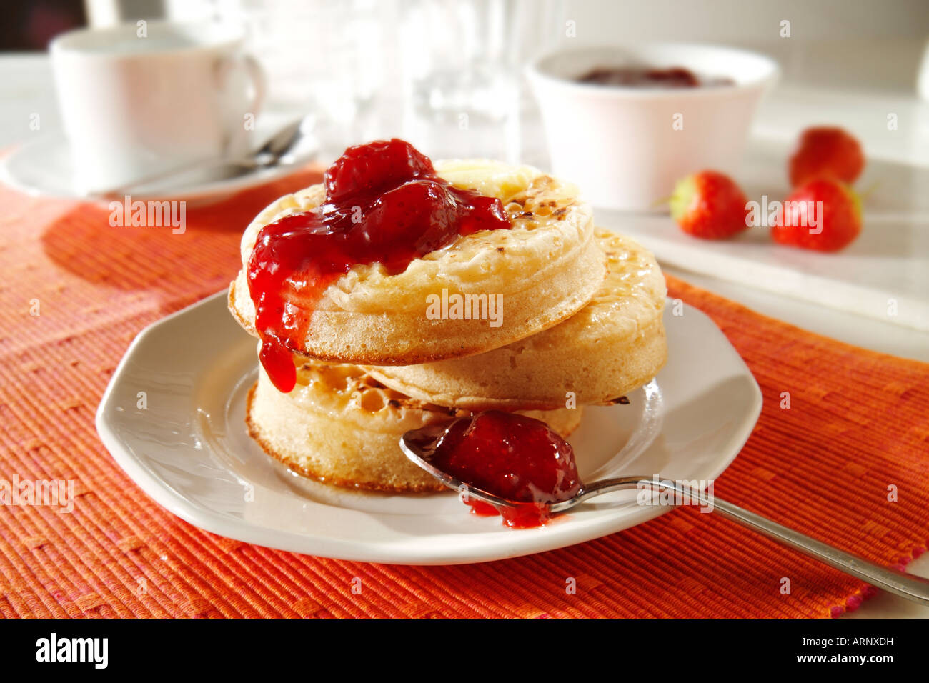 Close up de crumpets grillés beurrés avec de la confiture de fraise prêtes à manger dans un paramètre de table blanc Banque D'Images