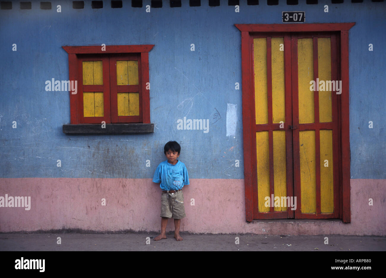 Garçon Maya de San Sebastian Retalhuleu se tient en dehors de son domicile peint de couleurs vives, côte du Pacifique au Guatemala Banque D'Images