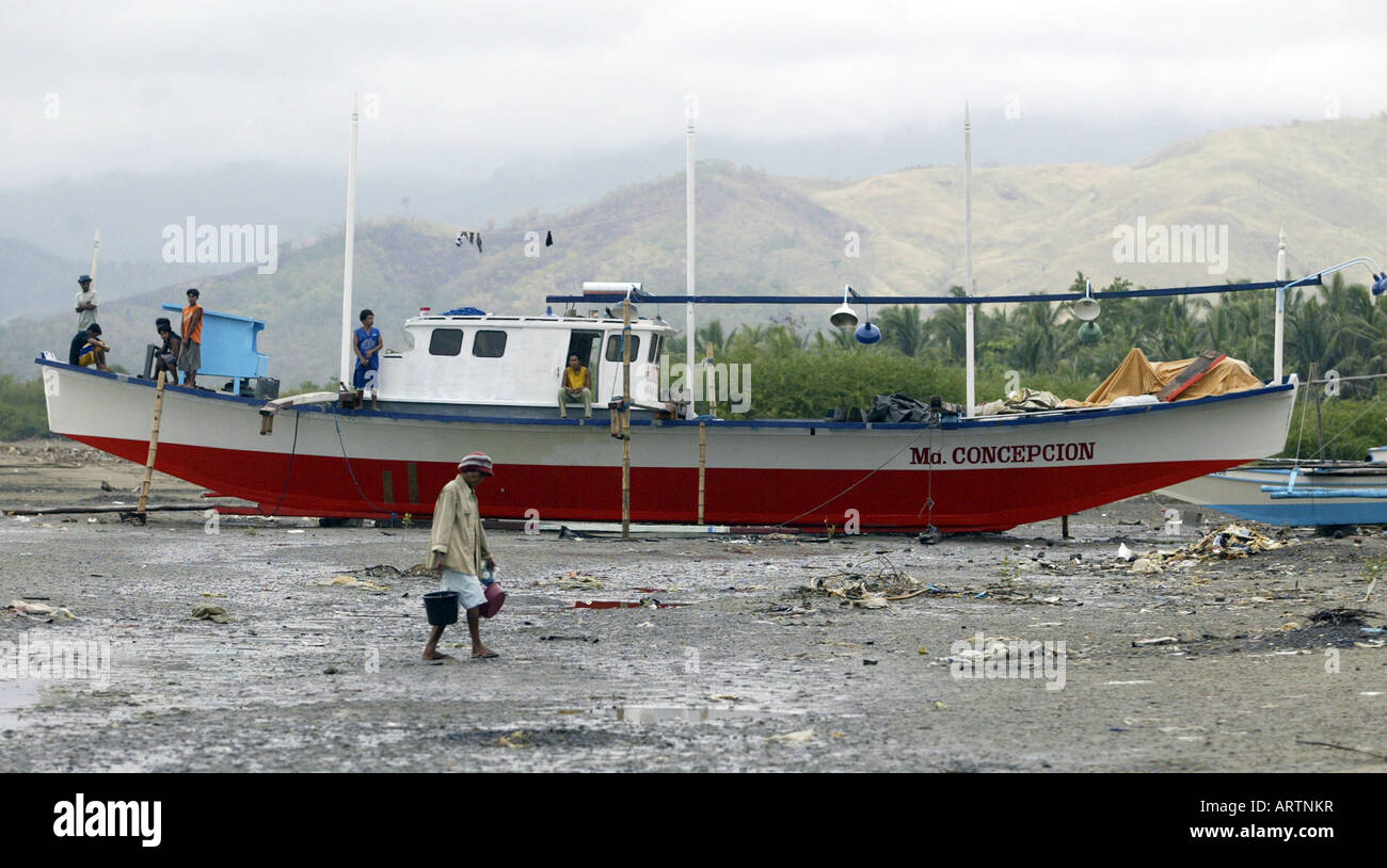 Pêcheurs attendent pour la vague à venir dans de lancer leur bateau sur une plage à Mansalay, Oriental Mindoro, Philippines. Banque D'Images