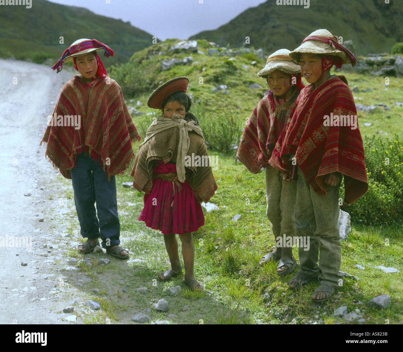Quatre enfants dans les Andes ponchos traditionnels accueillent les visiteurs sur une route de montagne dans les andes près de Cuzco au Pérou Banque D'Images