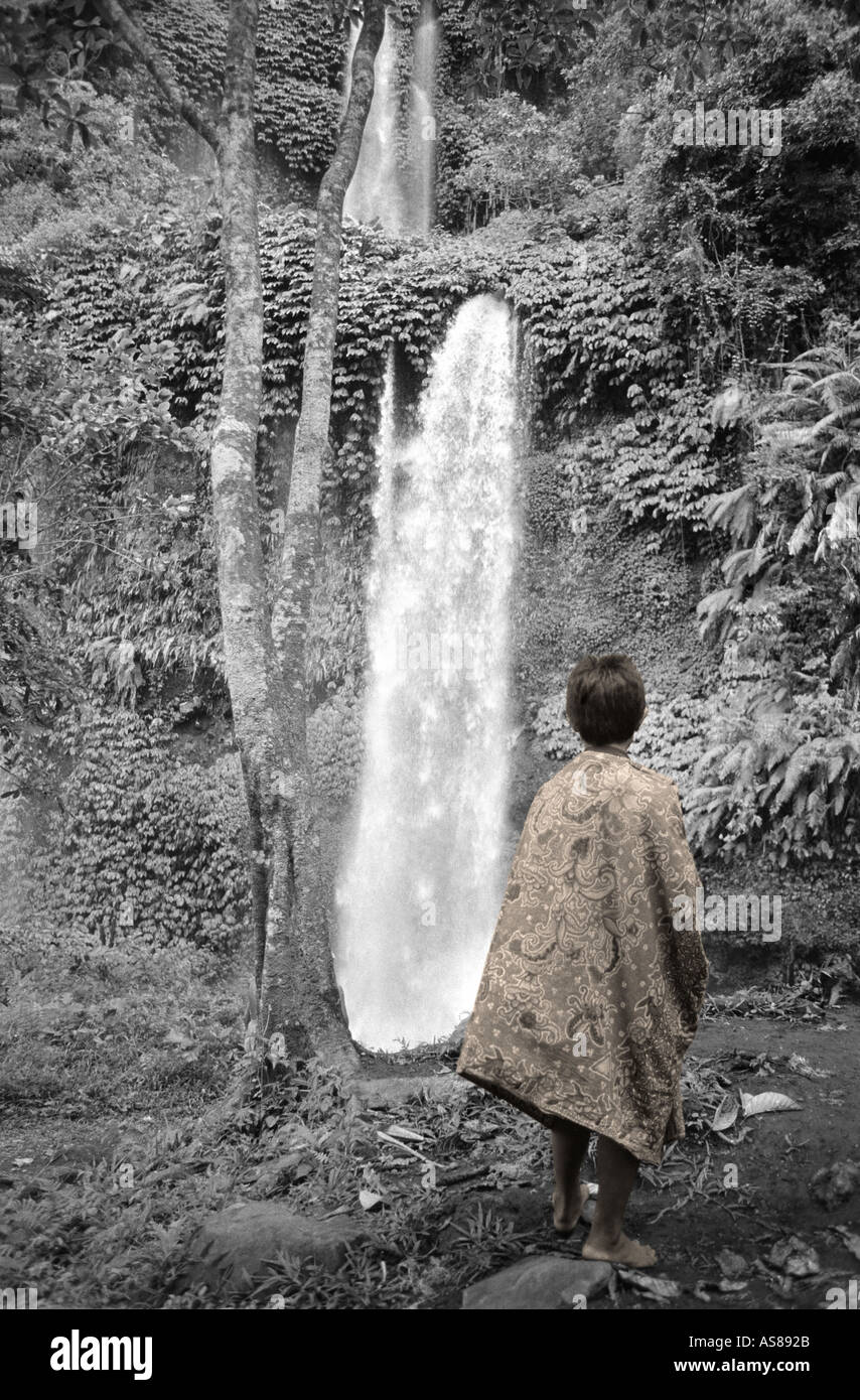 Garçon indonésien enveloppée dans un sarong debout devant le 40m de haut Cascade de Gitgit Lombok Indonésie Sepia Toning sélective Banque D'Images