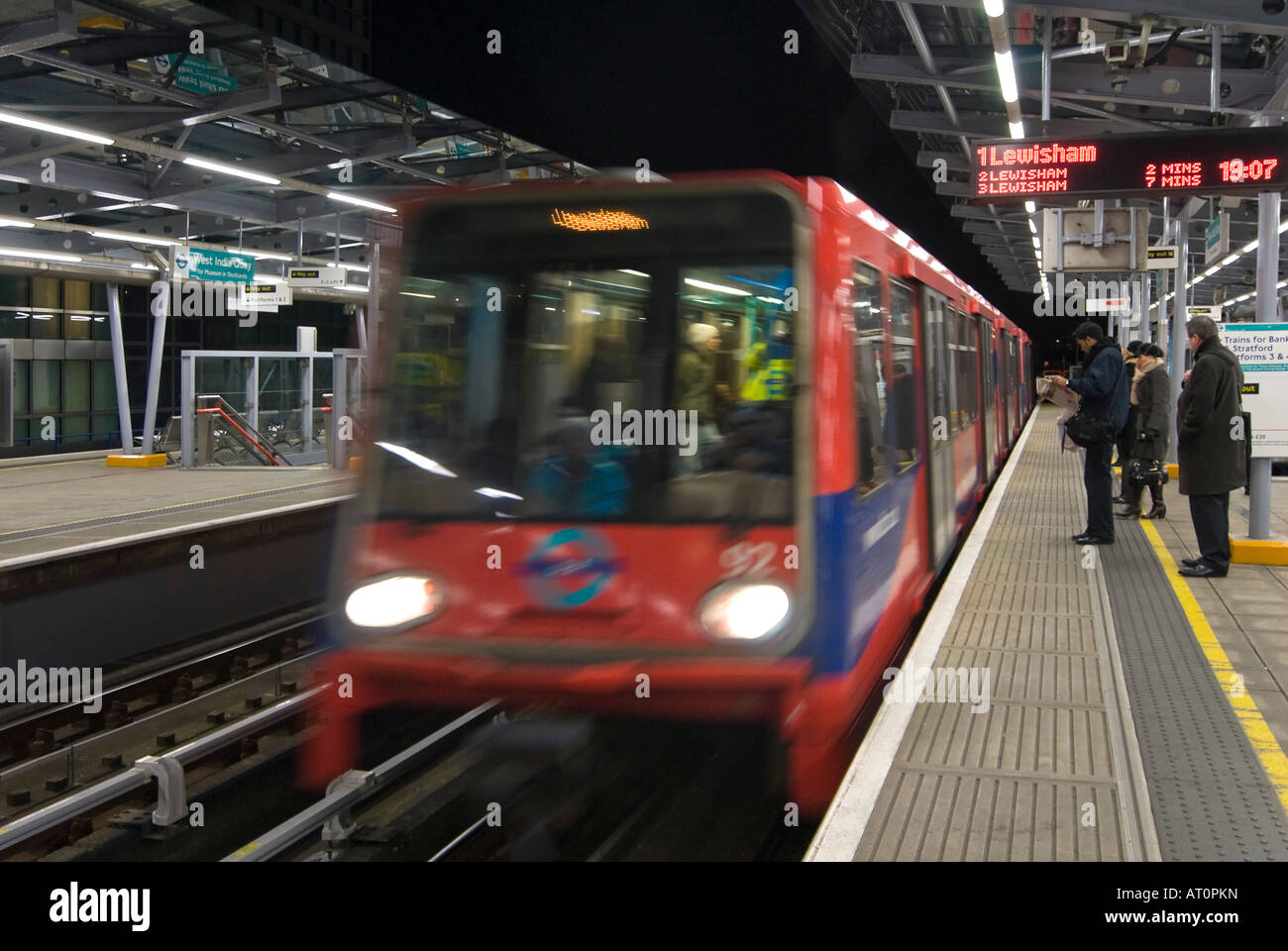 Grand angle horizontal d'un Docklands Light Railway train arrivant en gare de peuplier avec des gens qui attendent sur la plate-forme dans la nuit Banque D'Images