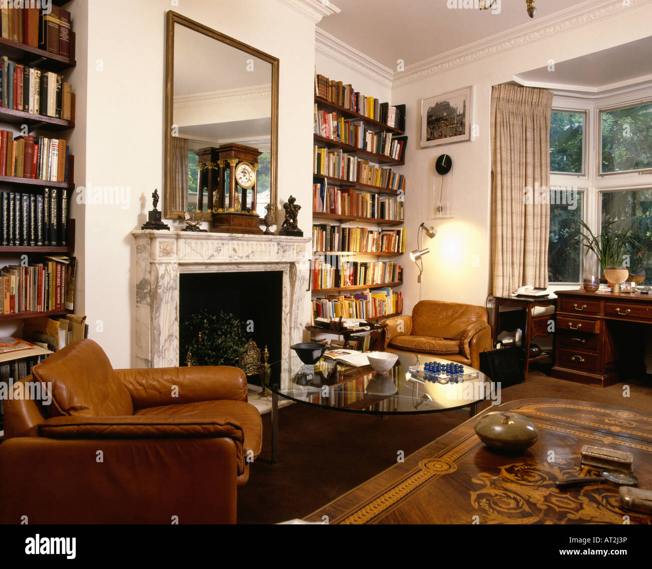 Les fauteuils en cuir marron 70 salon avec bibliothèque et un grand miroir au-dessus de cheminée en marbre Banque D'Images