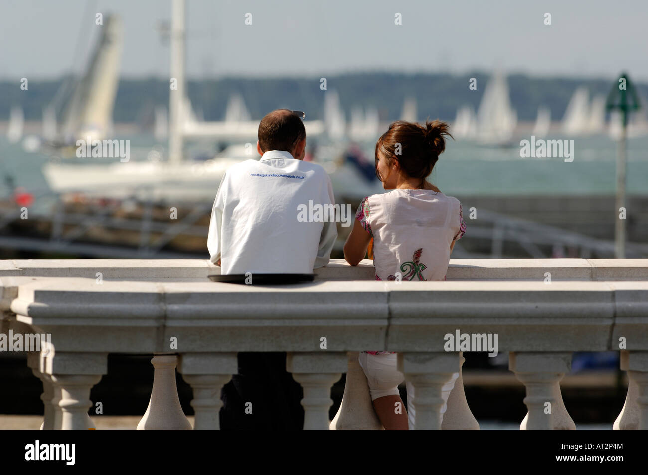 Un jeune couple partenaires hommes et femmes s'appuyant sur le mur de la mer sur l'esplanade en regardant le yacht racing au cours de la semaine de Cowes iow Banque D'Images