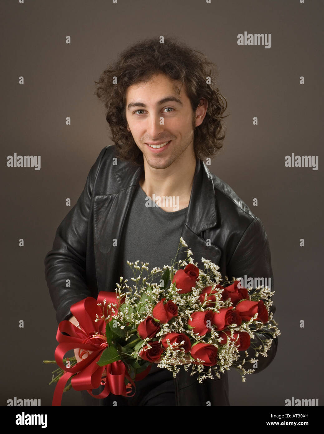 20 quelque chose smiling man l'homme à veste en cuir noire tenant une douzaine de roses rouges Banque D'Images