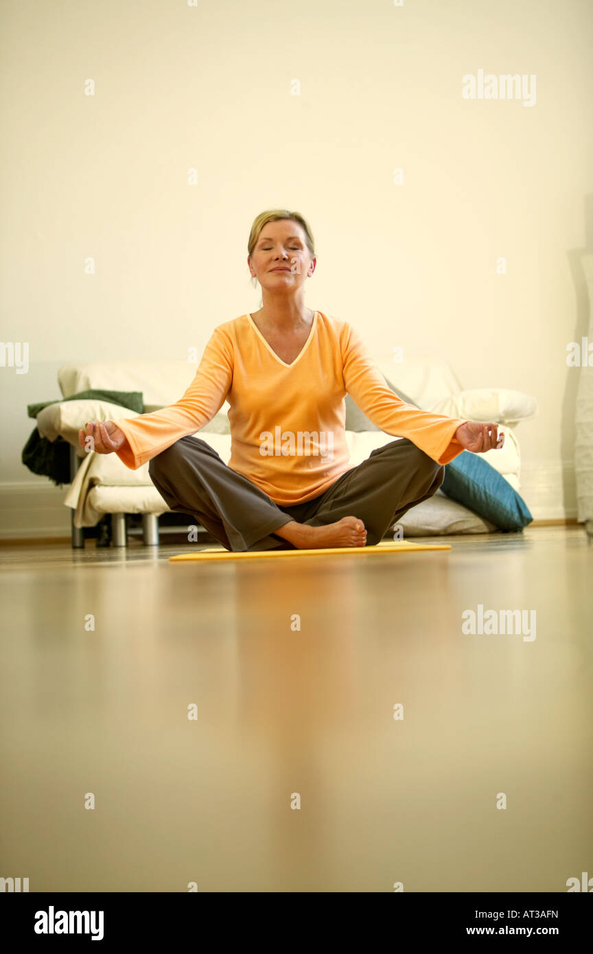 Une femme assise sur un tapis de yoga, méditant les yeux fermés Banque D'Images