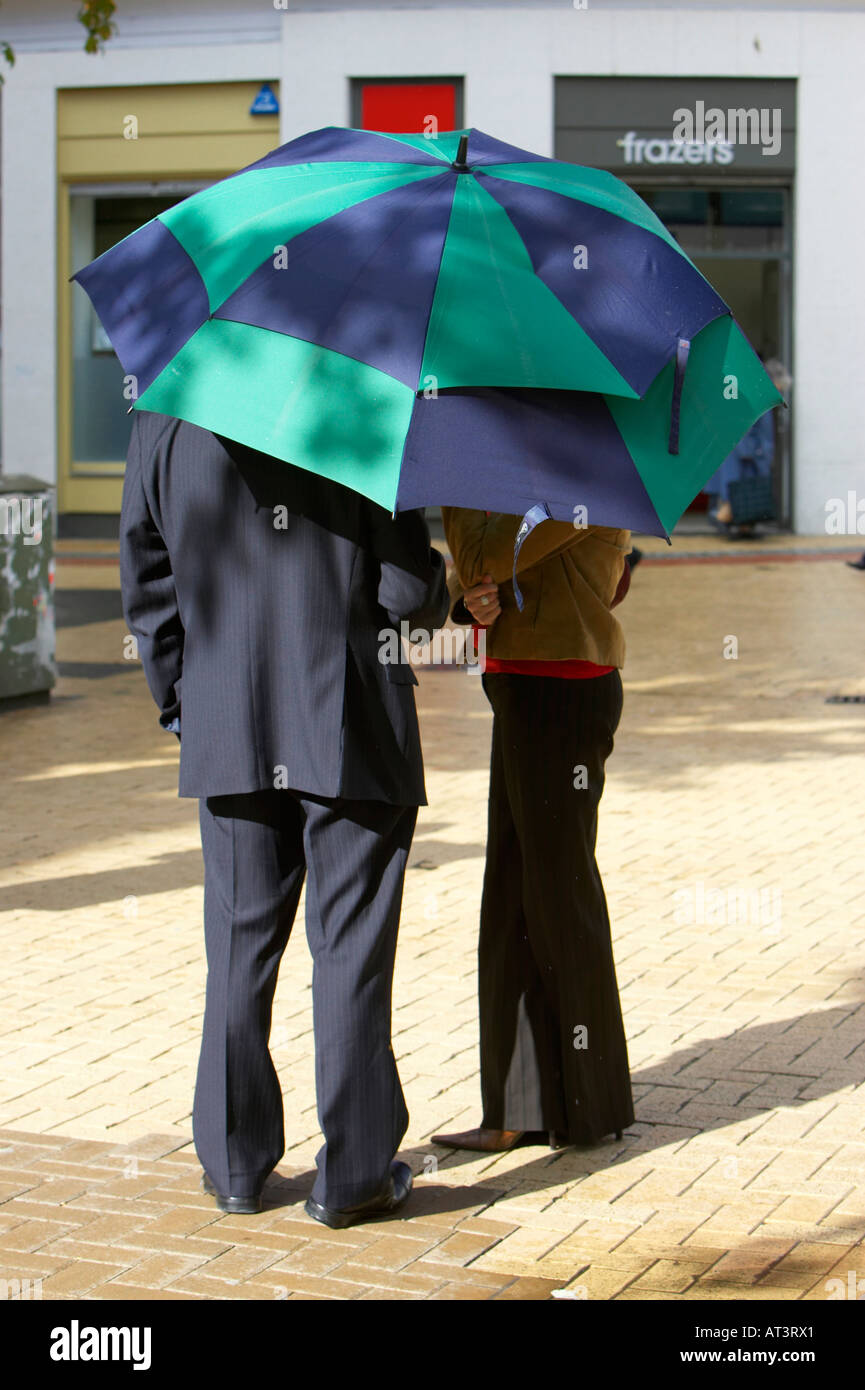 Homme en costume et une jeune femme debout sous un grand bleu et vert parapluie de golf en zone piétonne dans le centre-ville de Belfast Banque D'Images