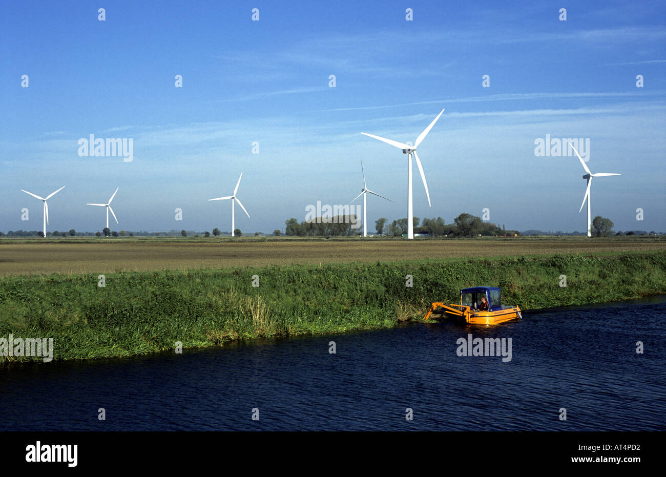 L'entretien de la banque de la rivière Nene en bateau aux éoliennes derrière sur les fens, près de mars, Cambridgeshire, Angleterre, RU Banque D'Images