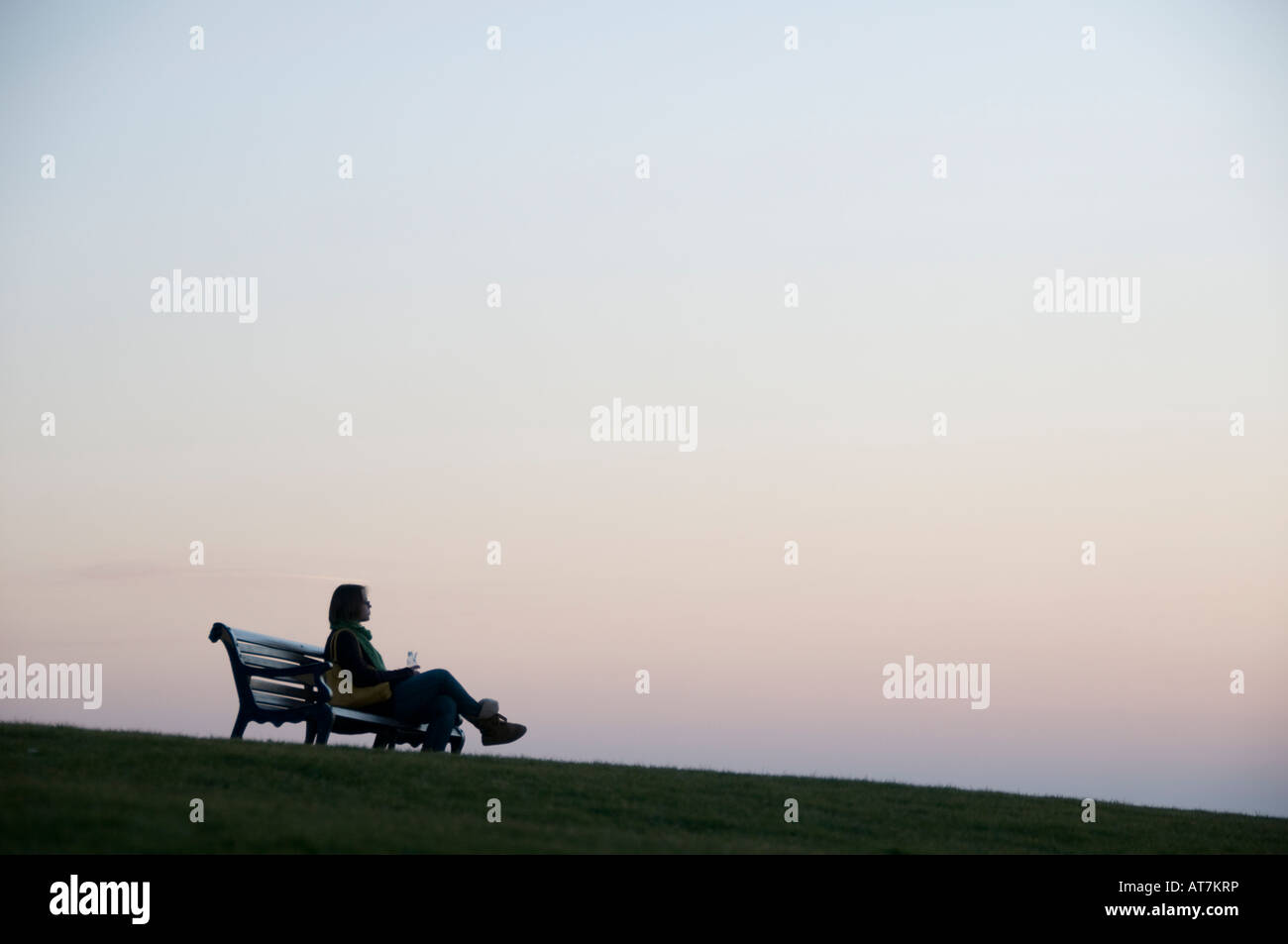 Femme assise seule par elle-même sur un banc de parc au crépuscule Aberystwyth Wales UK Banque D'Images