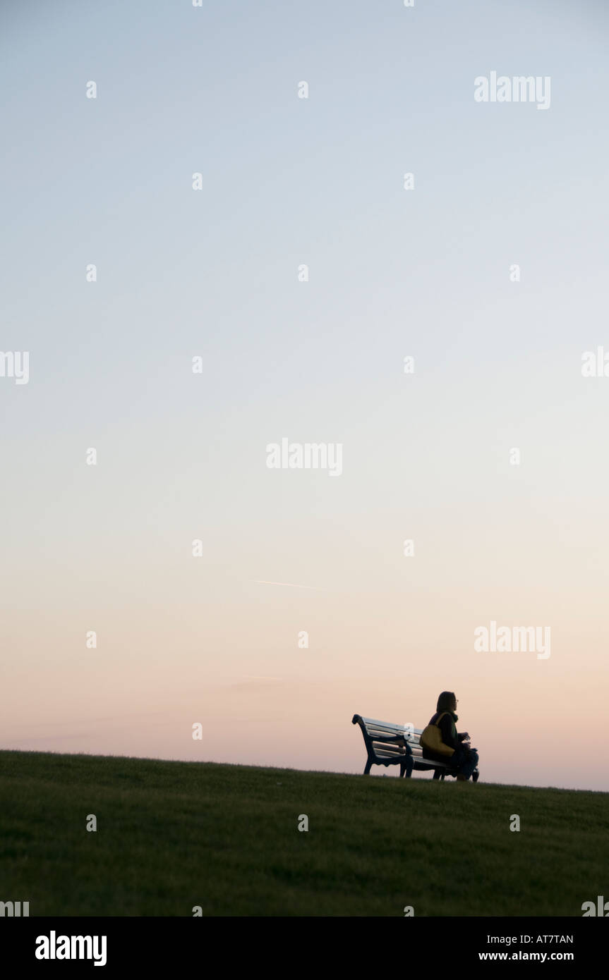 Femme assise seule par elle-même sur un banc de parc au crépuscule Aberystwyth Wales UK Banque D'Images
