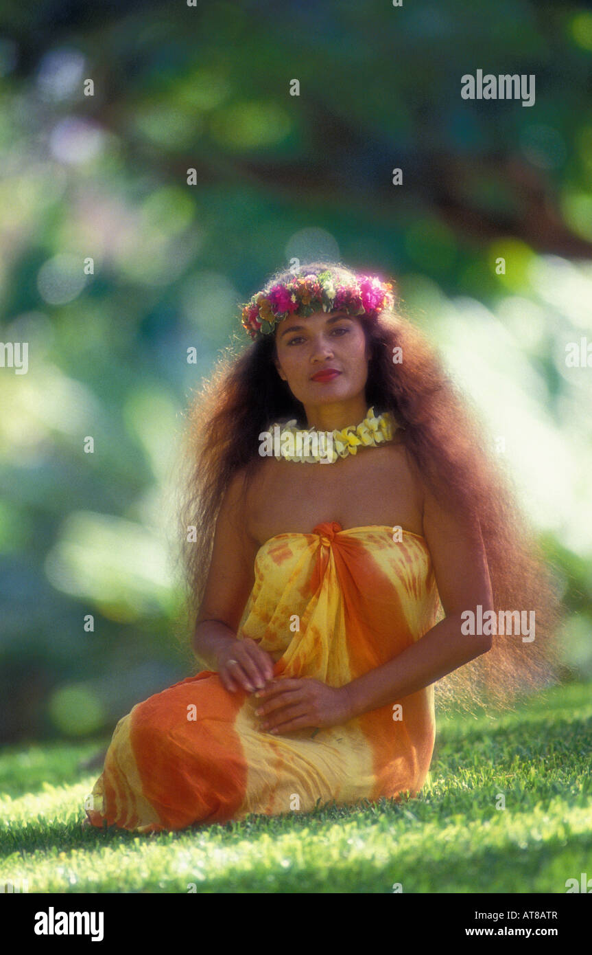 Belle femme polynésienne traditionnelle avec la longueur de la taille de l'herbe sèche assis sur le port d'un paréo orange et jaune, plumeria lei Banque D'Images