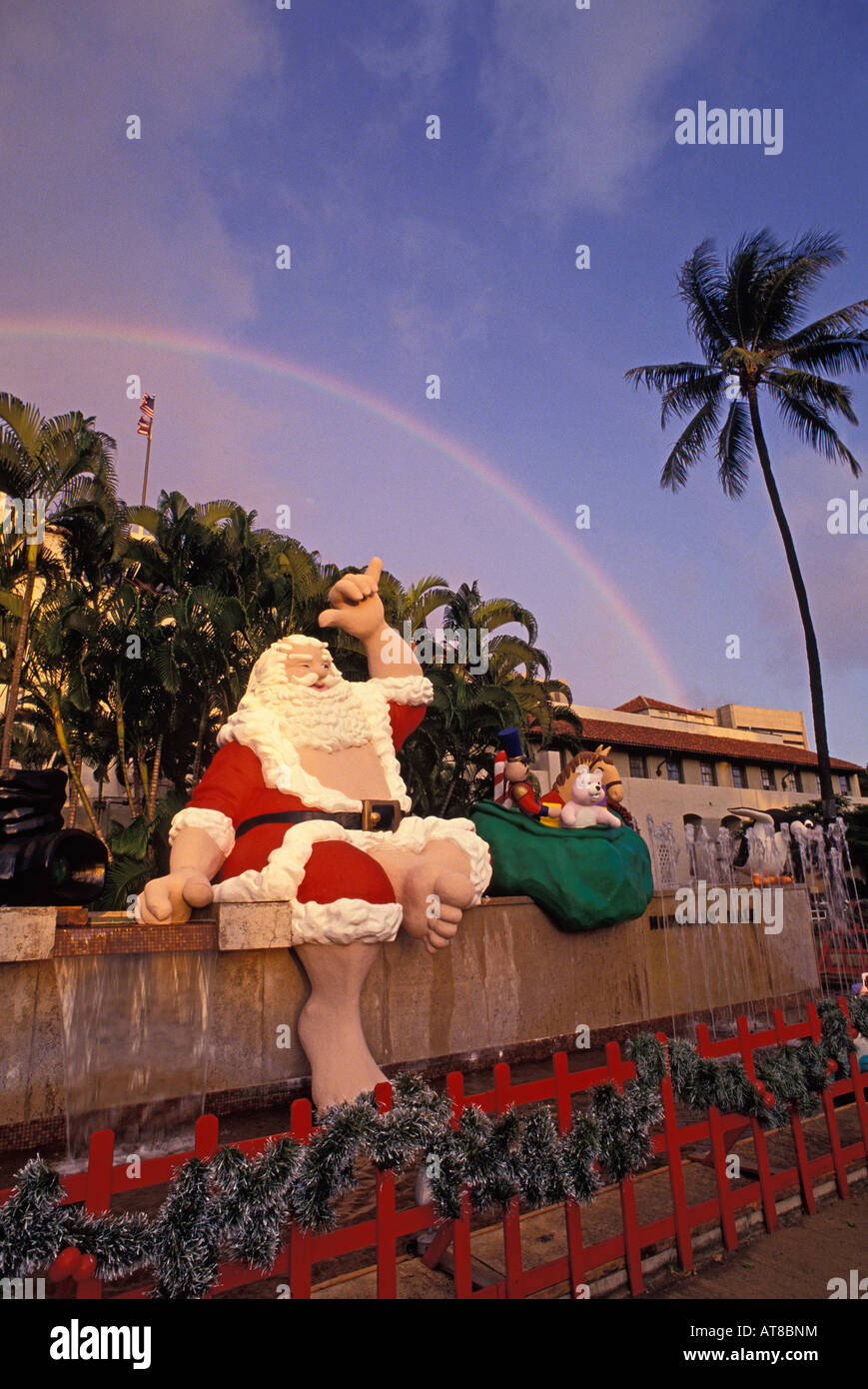 Grand Père Noël assis sur le mur extérieur à Honolulu Hale signe shaka  clignotant avec un arc-en-ciel en arrière-plan Photo Stock - Alamy