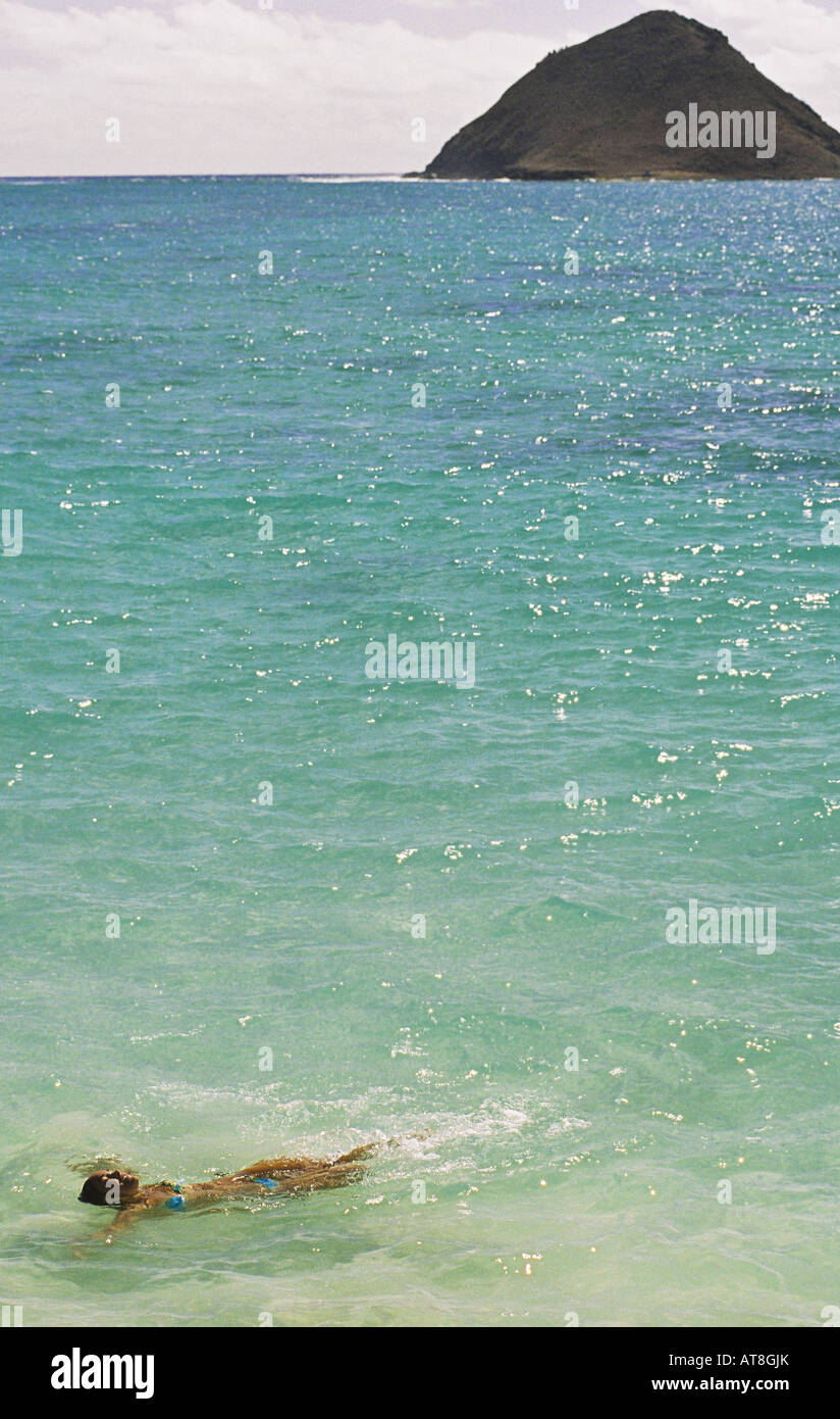 Jeune femme flottant dans l'océan à Lanikai beach, Oahu avec l'arrière de l'île en lua moku Banque D'Images