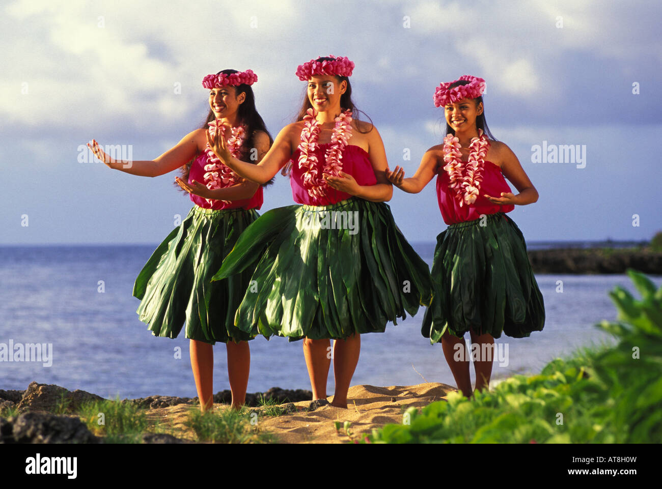 Trois danseurs hula avec plumeria leis et ti jupes de feuilles près de ocean Banque D'Images