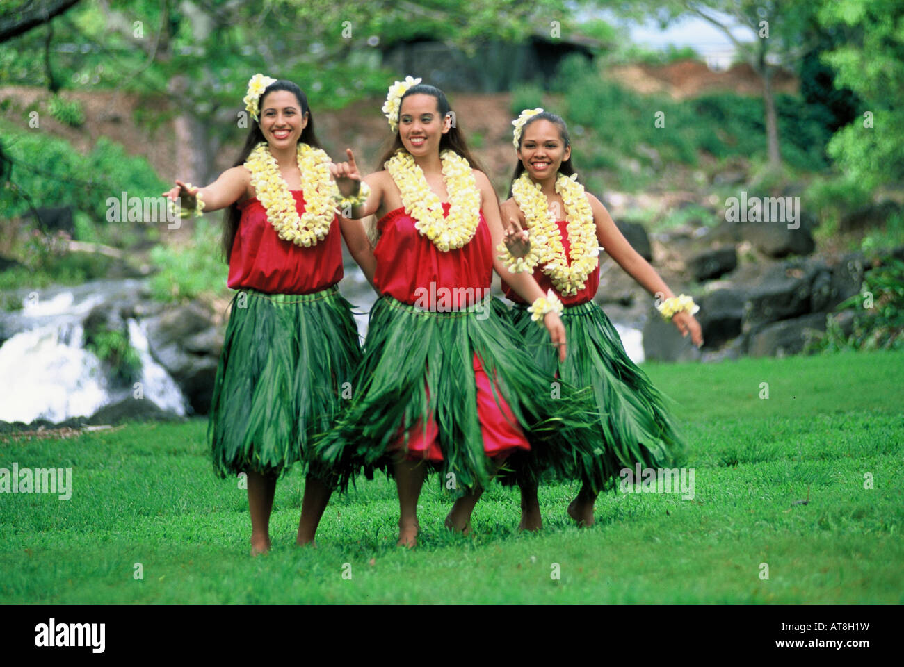 Trois danseurs hula près de Cascade de feuilles de ti jupes et yellow plumeria leis Banque D'Images