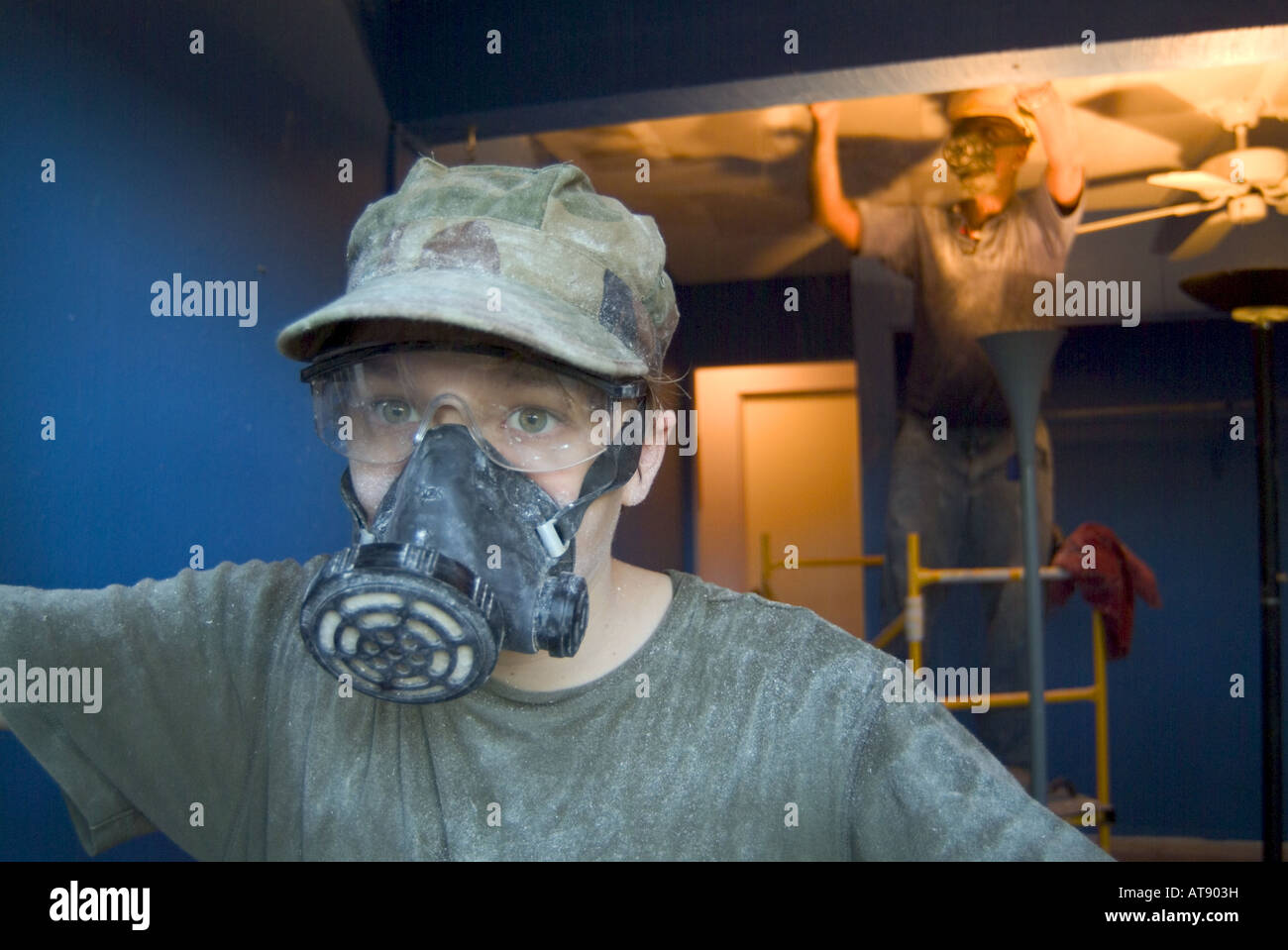 Accueil Travaux de construction. Le port d'un masque de ventalation adolescent tout en aidant à gratter le plafond avec plus african american man Banque D'Images